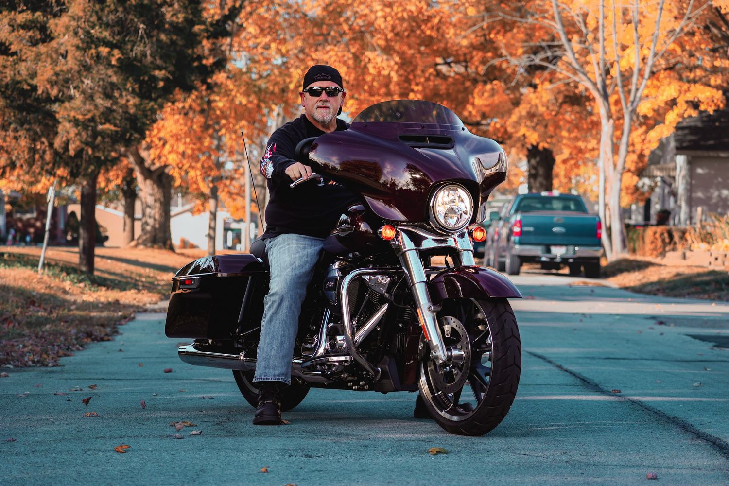 Purple Harley Davidson motorcycle parked on autumn street with rider in casual wear.