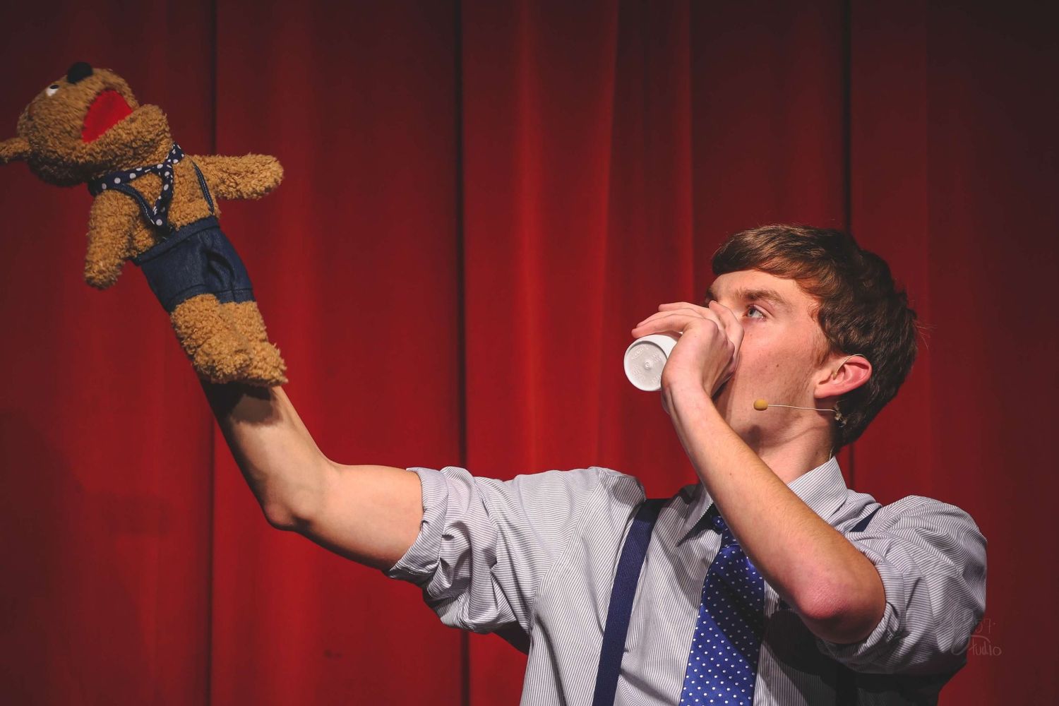 Person in business attire performing exaggerated expressions against a red curtain backdrop.