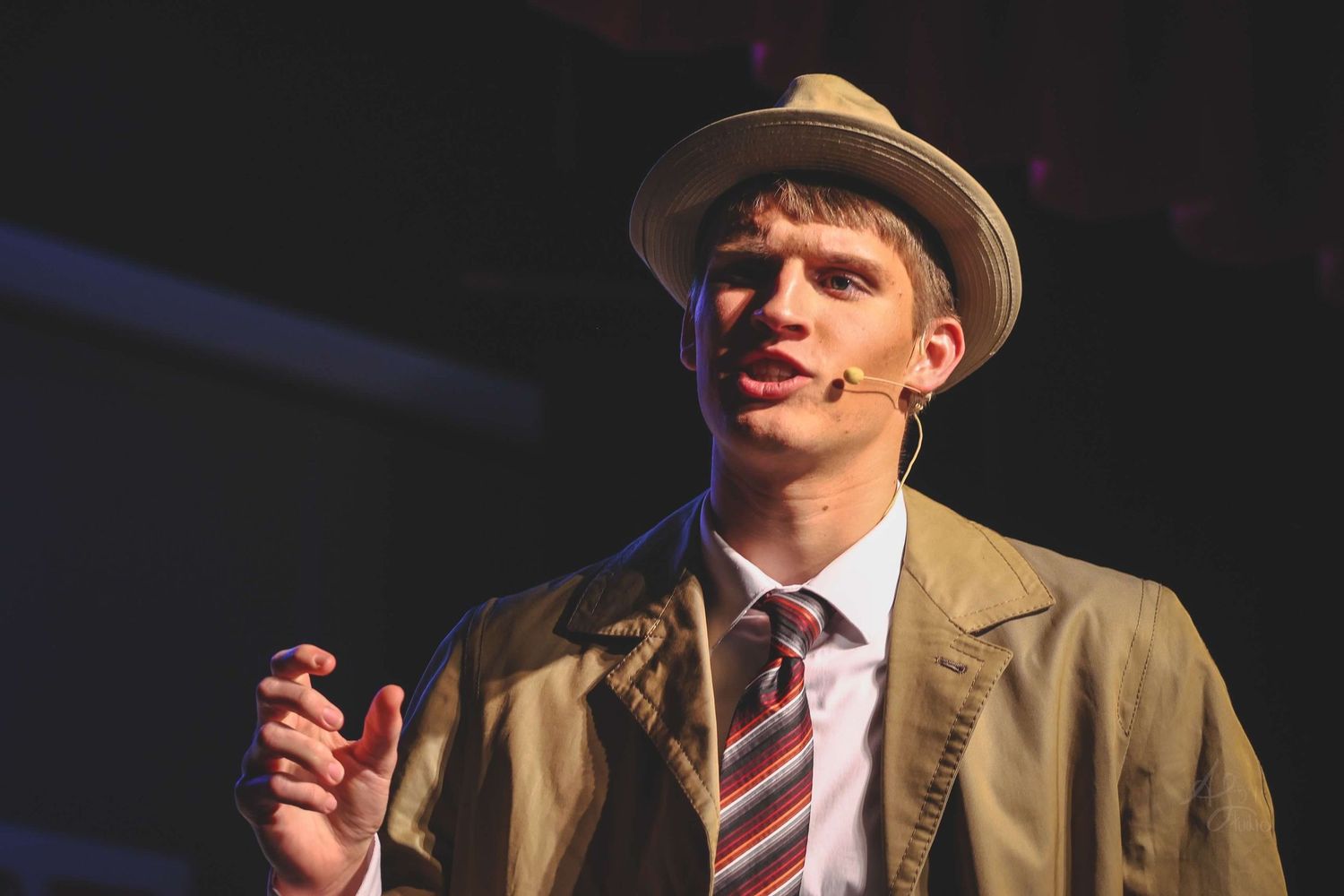 Performer in vintage attire and hat on stage under dramatic lighting.