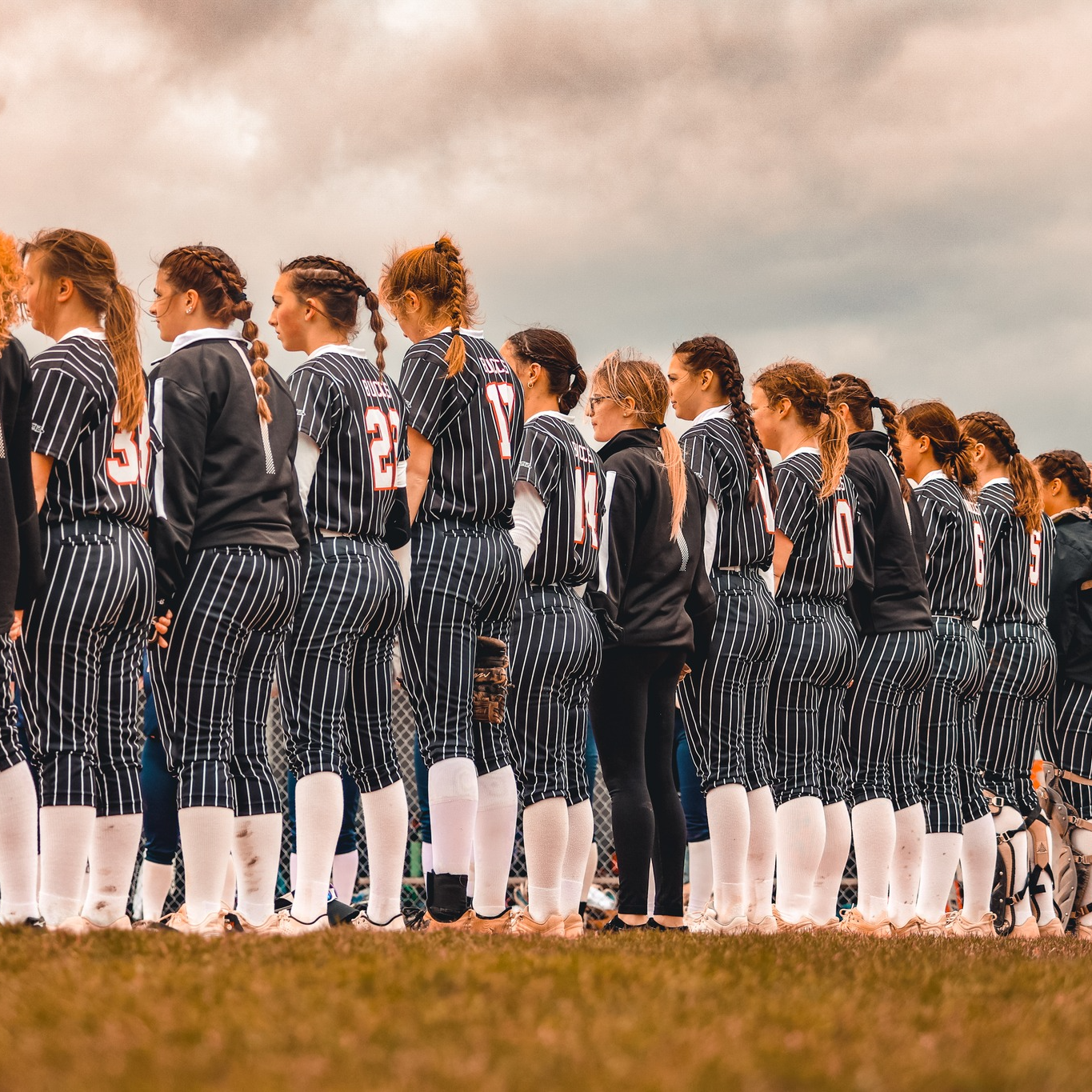 Softball team in pinstriped uniforms lined up on field at sunset.