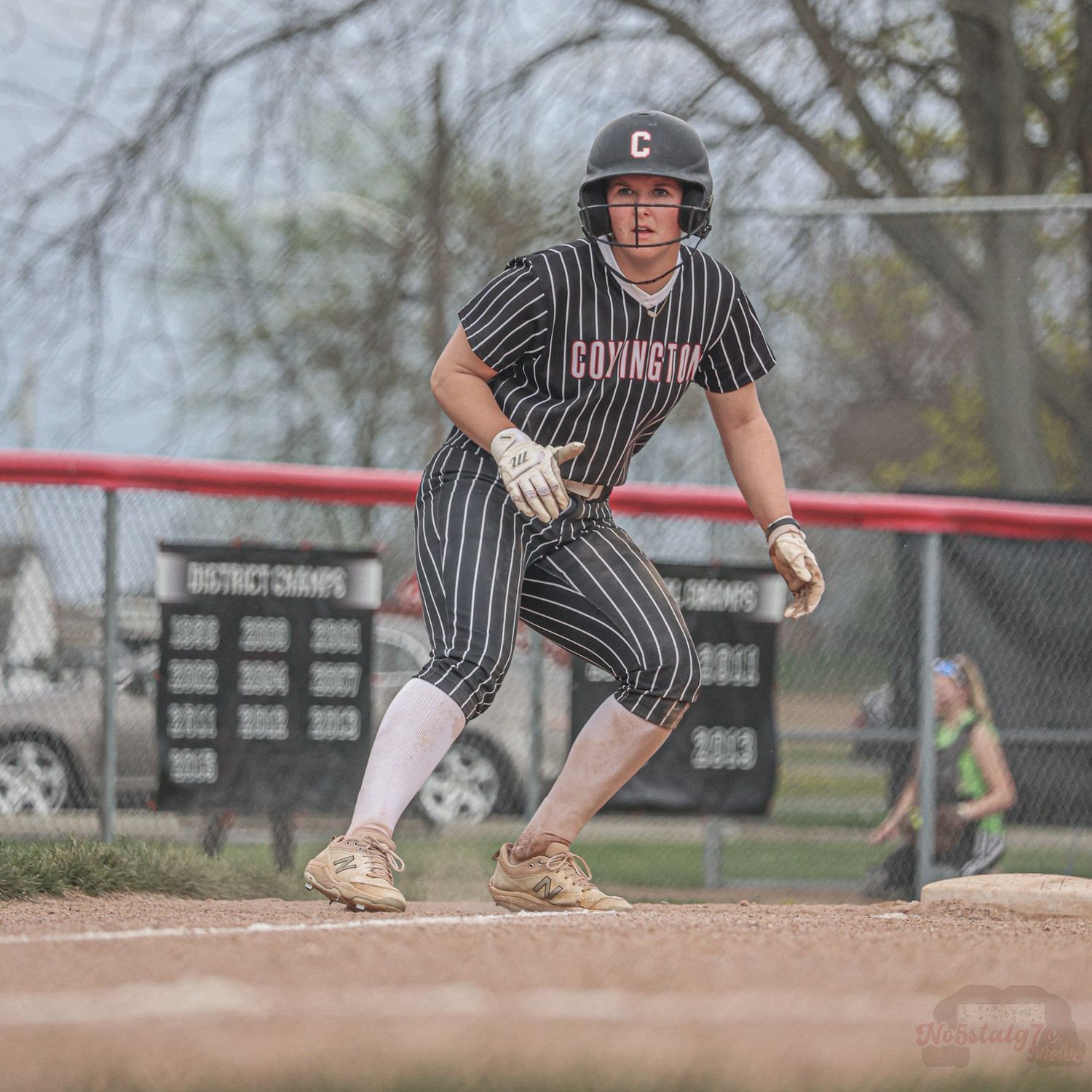 Baseball player in pinstripe uniform leads off from base during game.