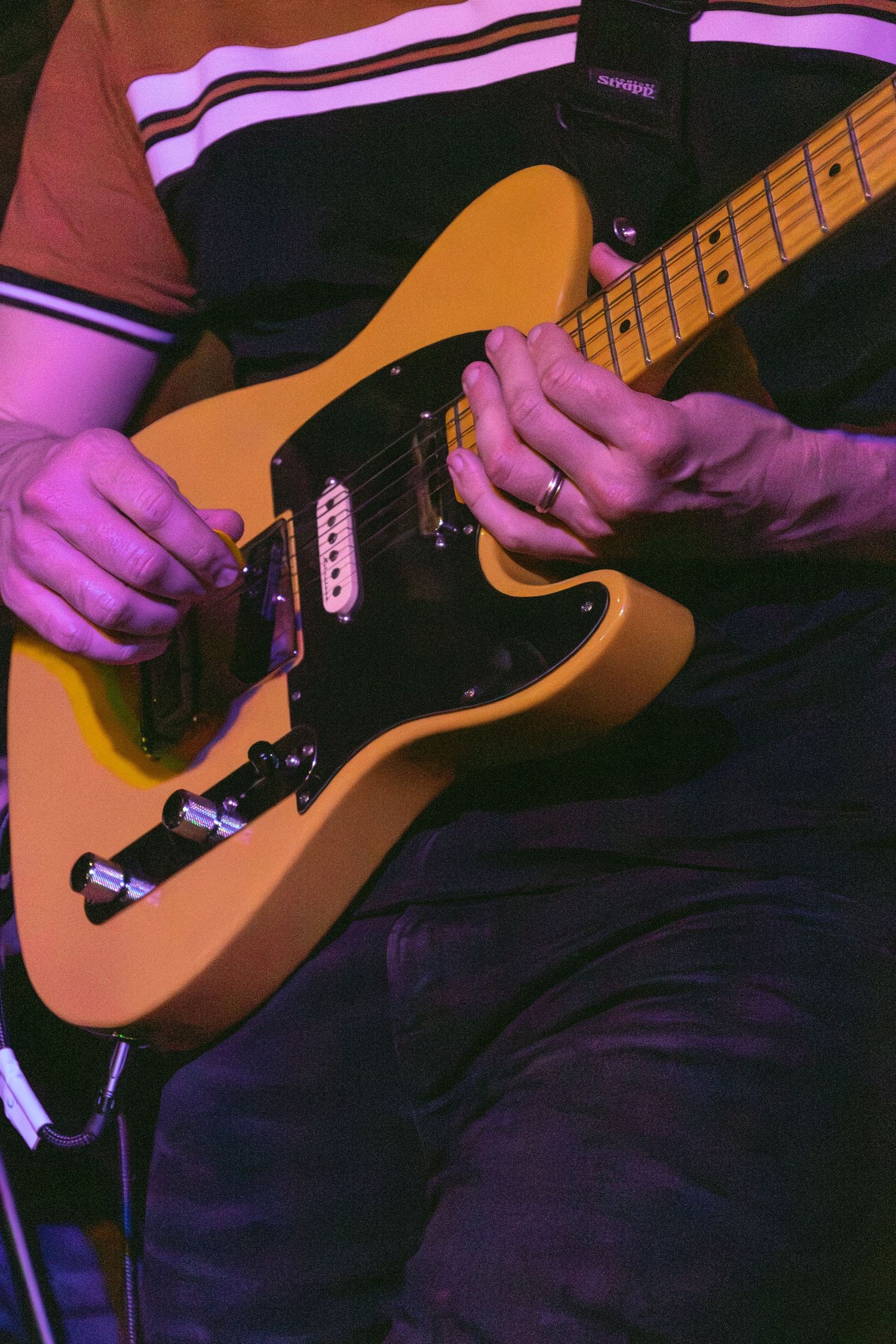 Musician playing a butterscotch Fender Telecaster electric guitar under purple stage lighting.