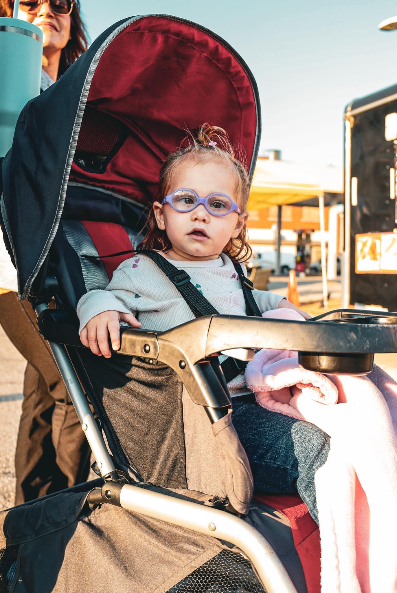 Baby in a red stroller during a sunny day at an outdoor event.