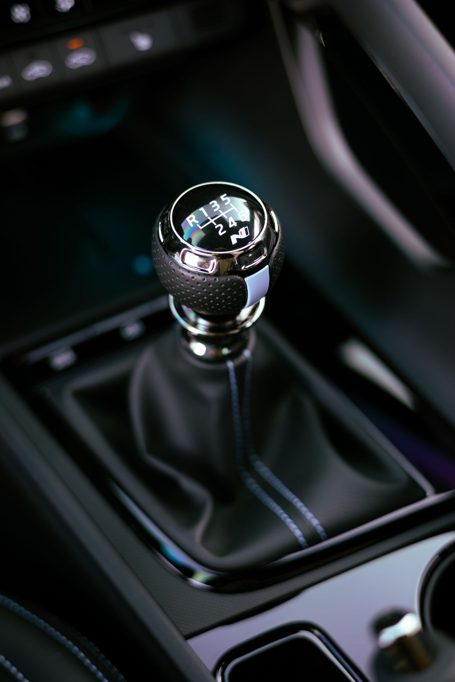 Close-up of a 6-speed manual gear shift knob with chrome accents in a modern car interior.