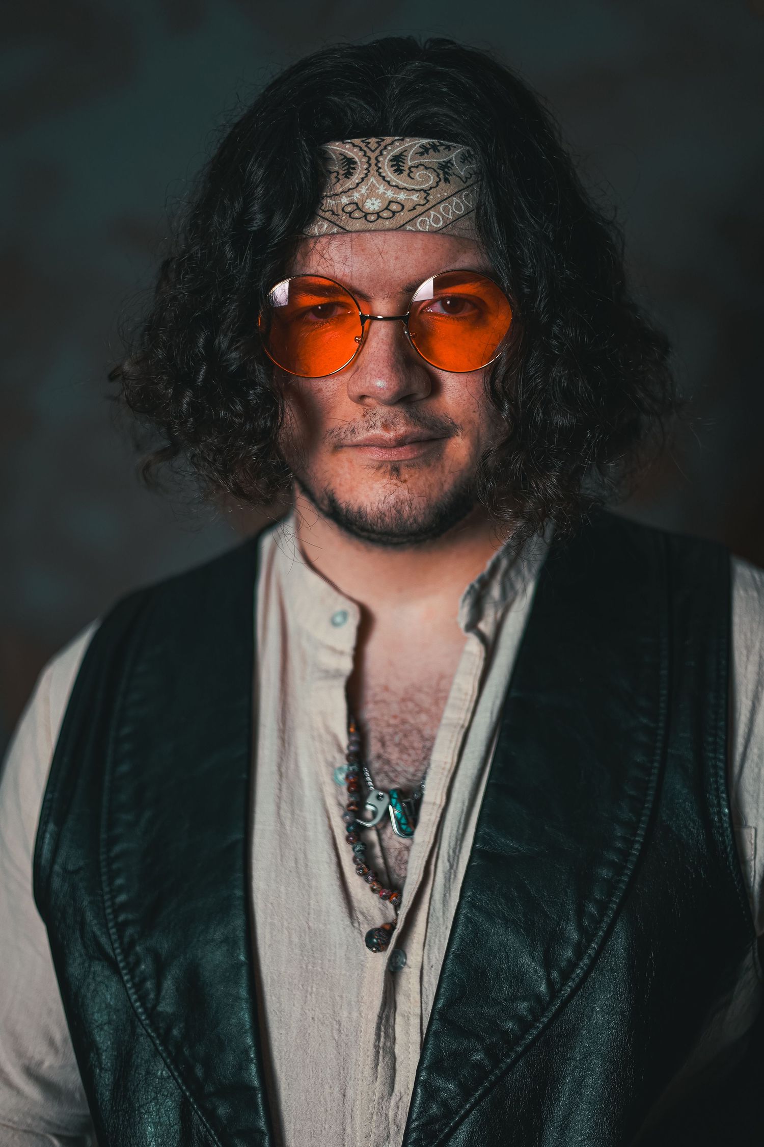 Portrait of a bohemian style person wearing orange tinted sunglasses and a bandana with curly dark hair.