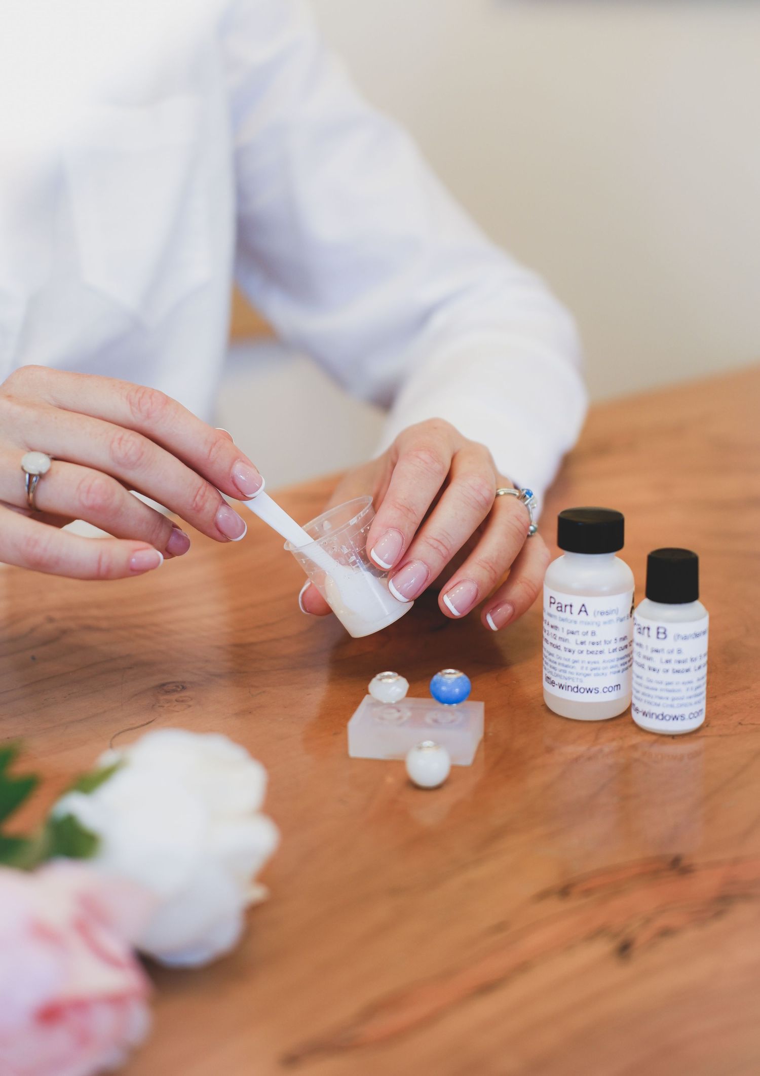 Close-up of hands mixing resin in a silicone mold with Part A and B solution bottles on a wooden table.