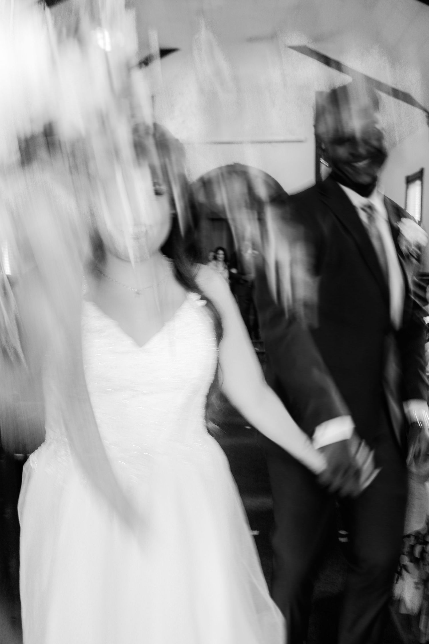 Black and white motion blur photo of a bride and groom holding hands walking together after their wedding ceremony.