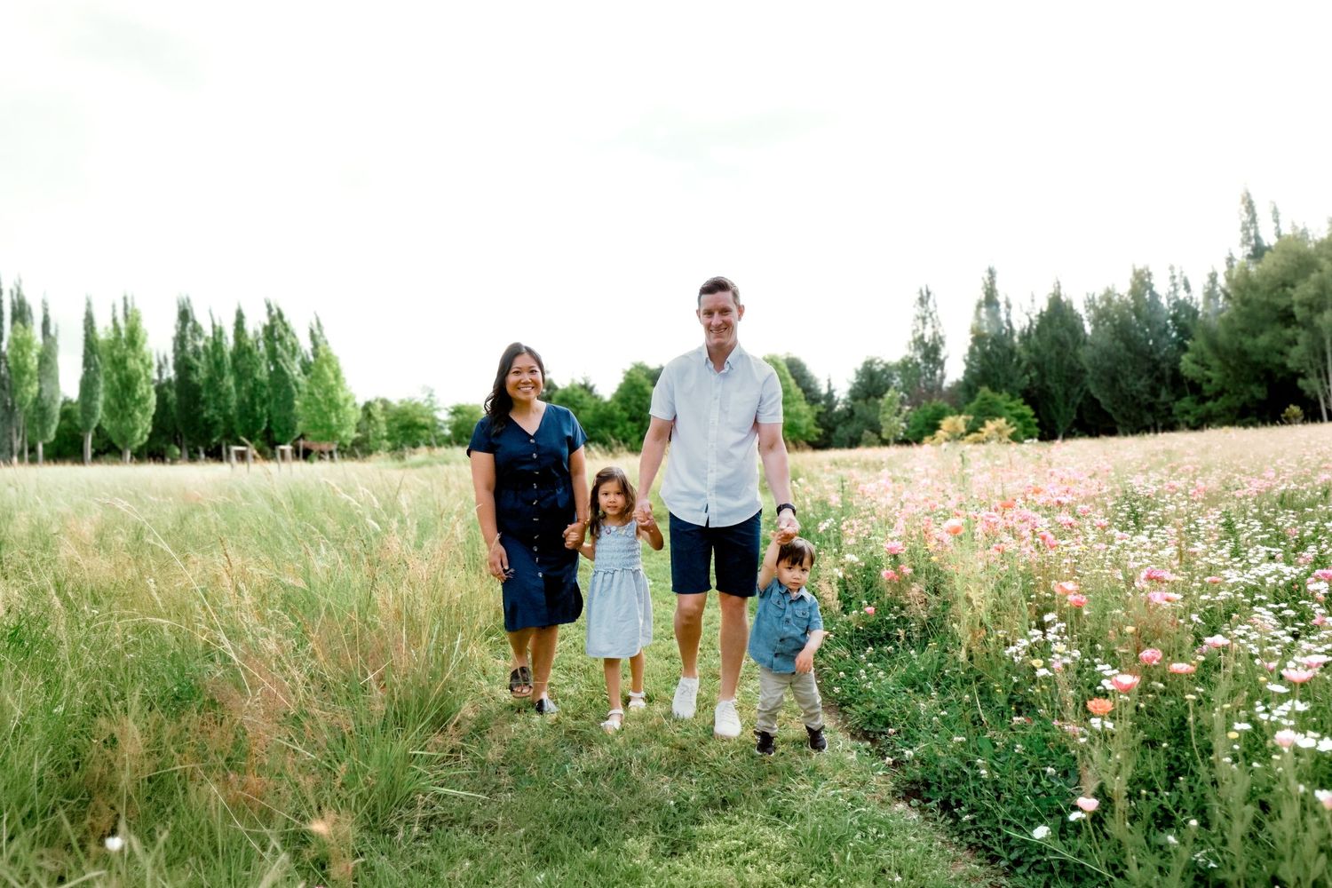 Family of four posing in a wildflower meadow with tall trees in background on a cloudy day.