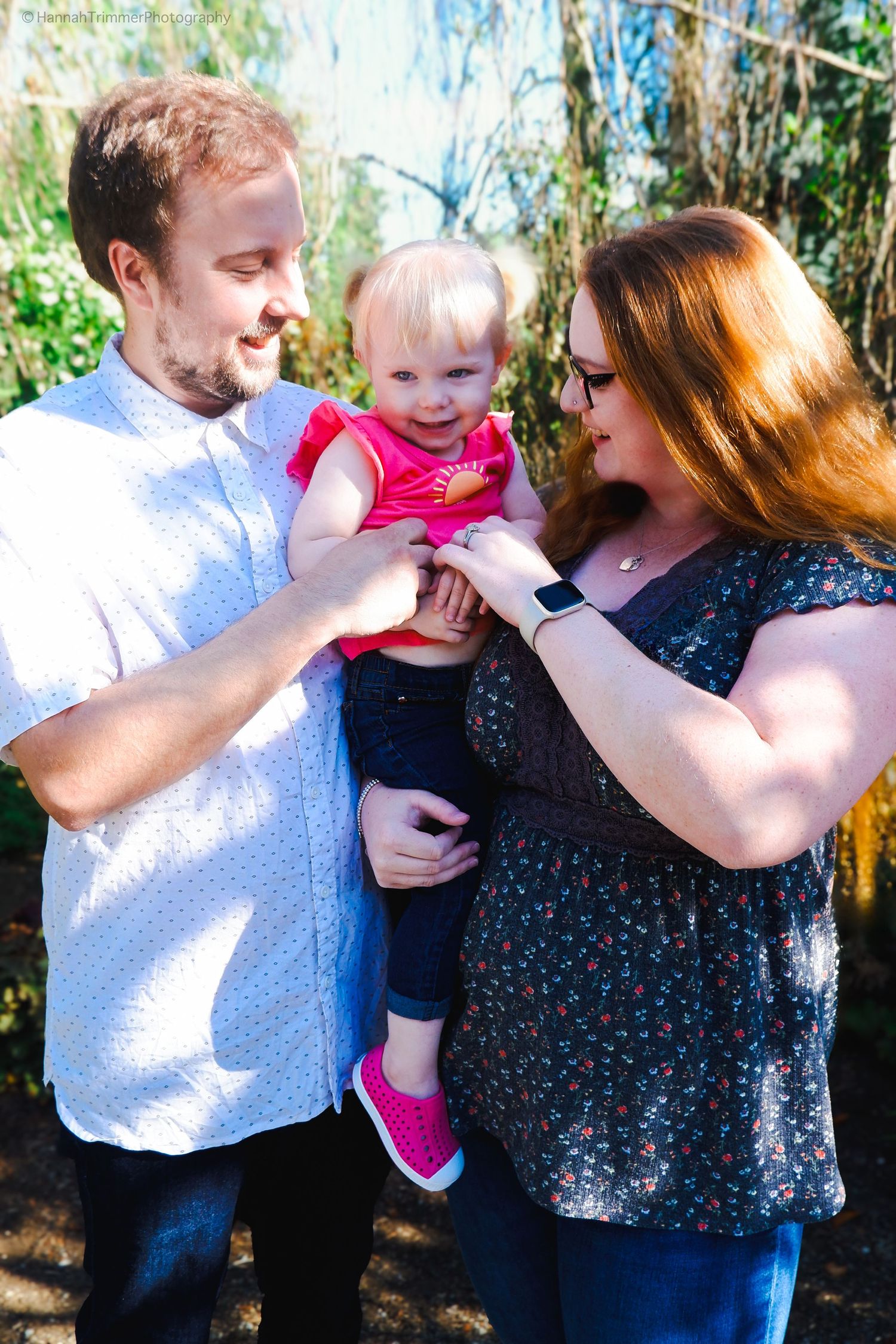 Young family with redhead mother, bearded father, and baby girl outdoors.