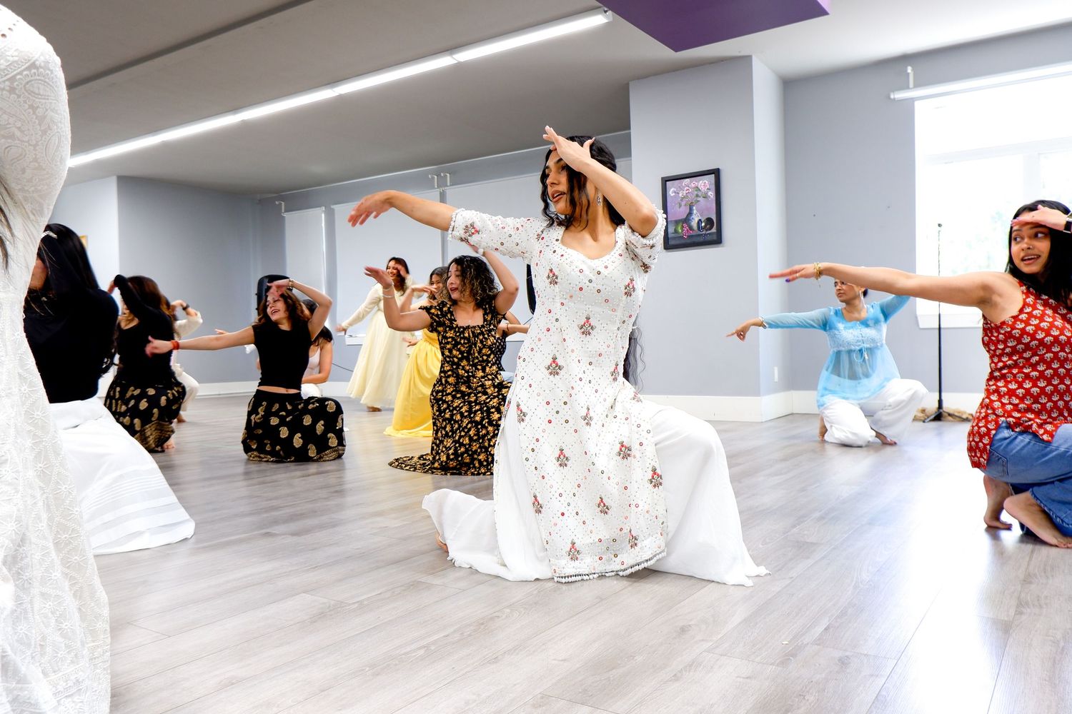 Group of women in colorful traditional Indian attire dancing in a bright modern studio.