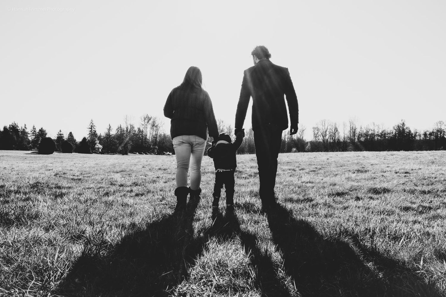Silhouette of a family of three holding hands while walking through an open field at sunset.
