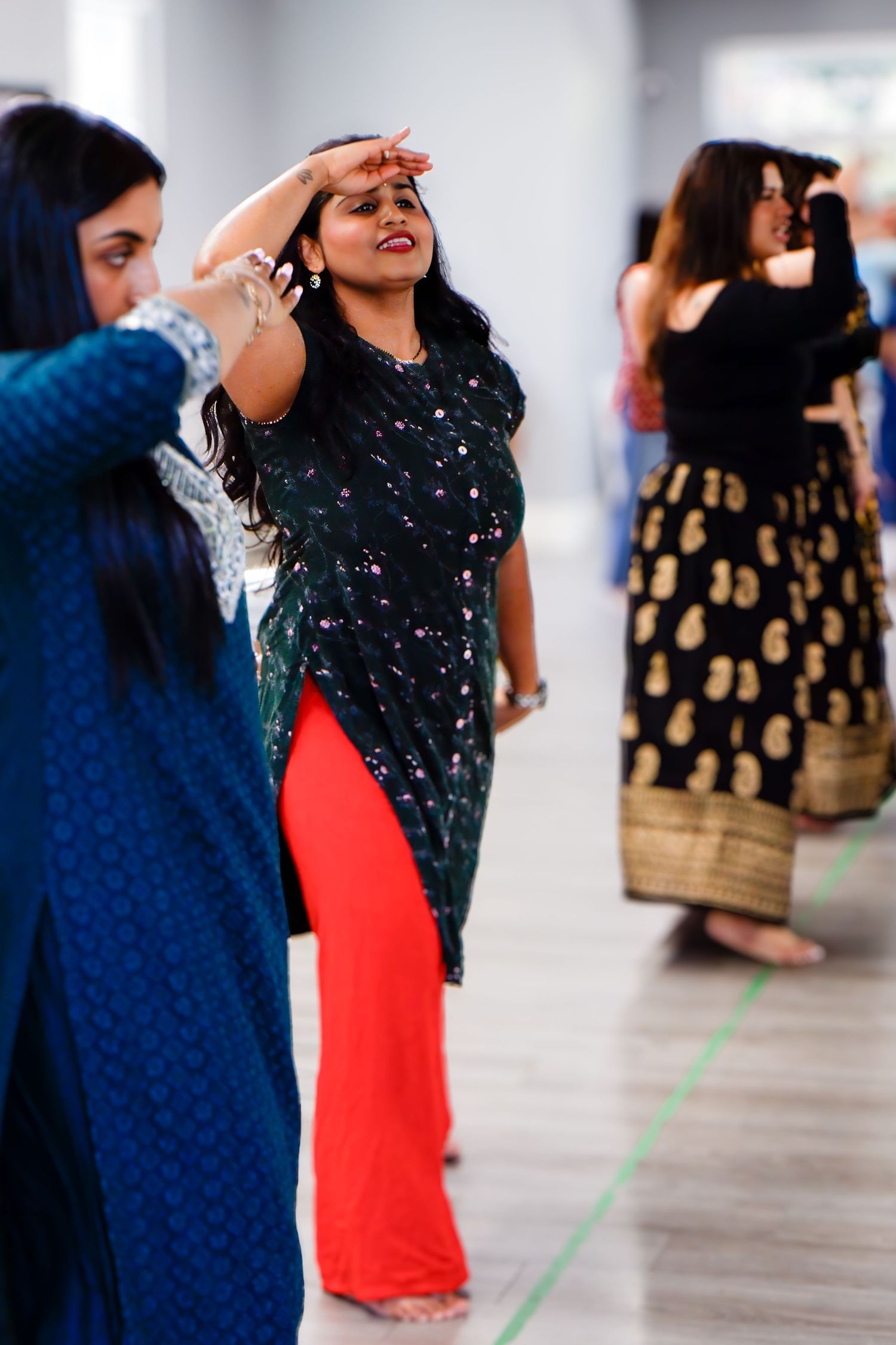 Women in traditional South Asian clothing practicing dance moves in a spacious studio.