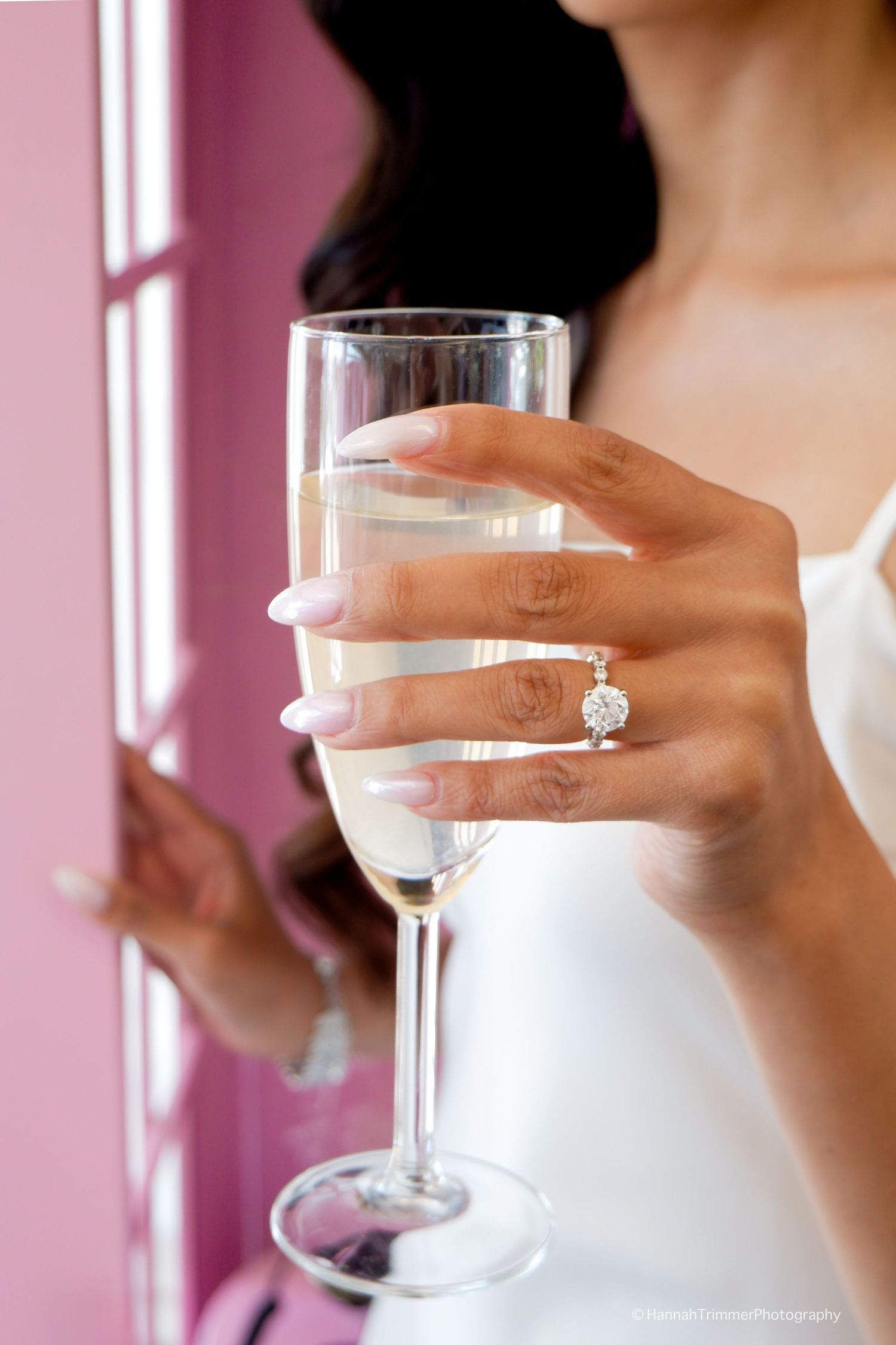 Bride to be holding a champagne flute showcasing a stunning diamond engagement ring at her bridal shower.