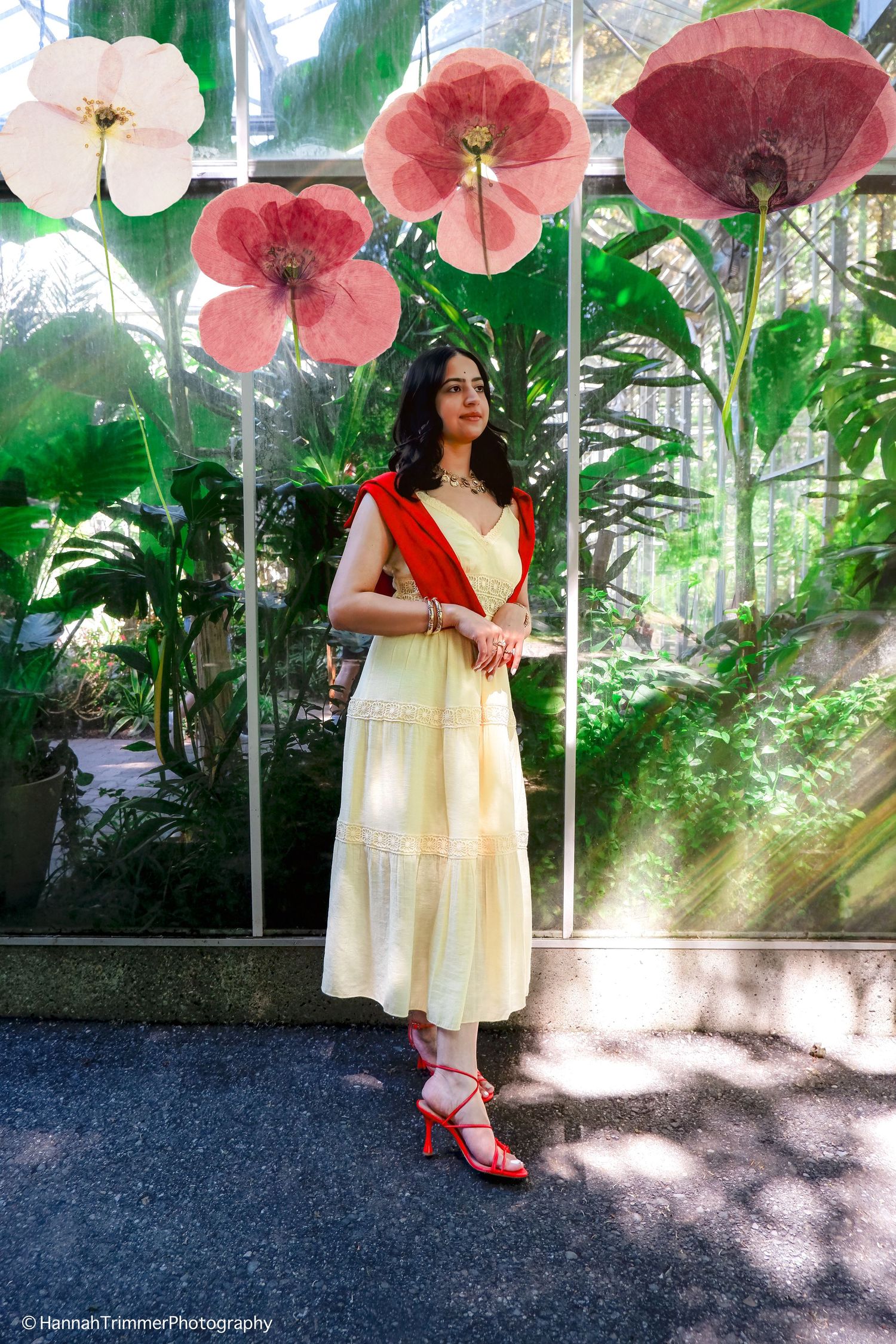 Woman in yellow dress and red heels posing in front of floral greenhouse display.