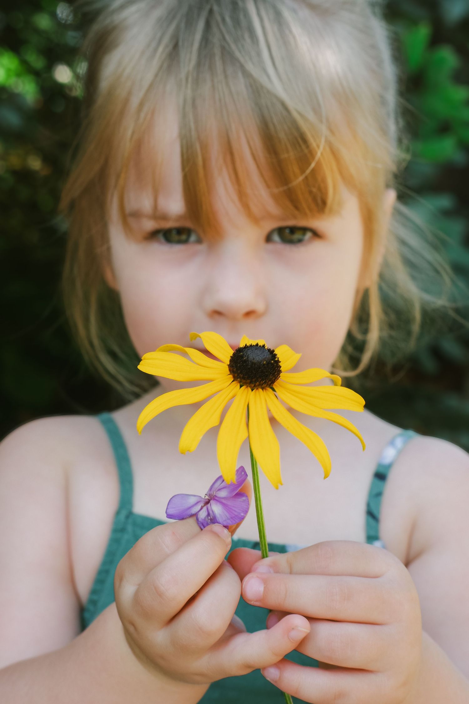 Young blonde girl holding a yellow black-eyed Susan flower close to her face outdoors.