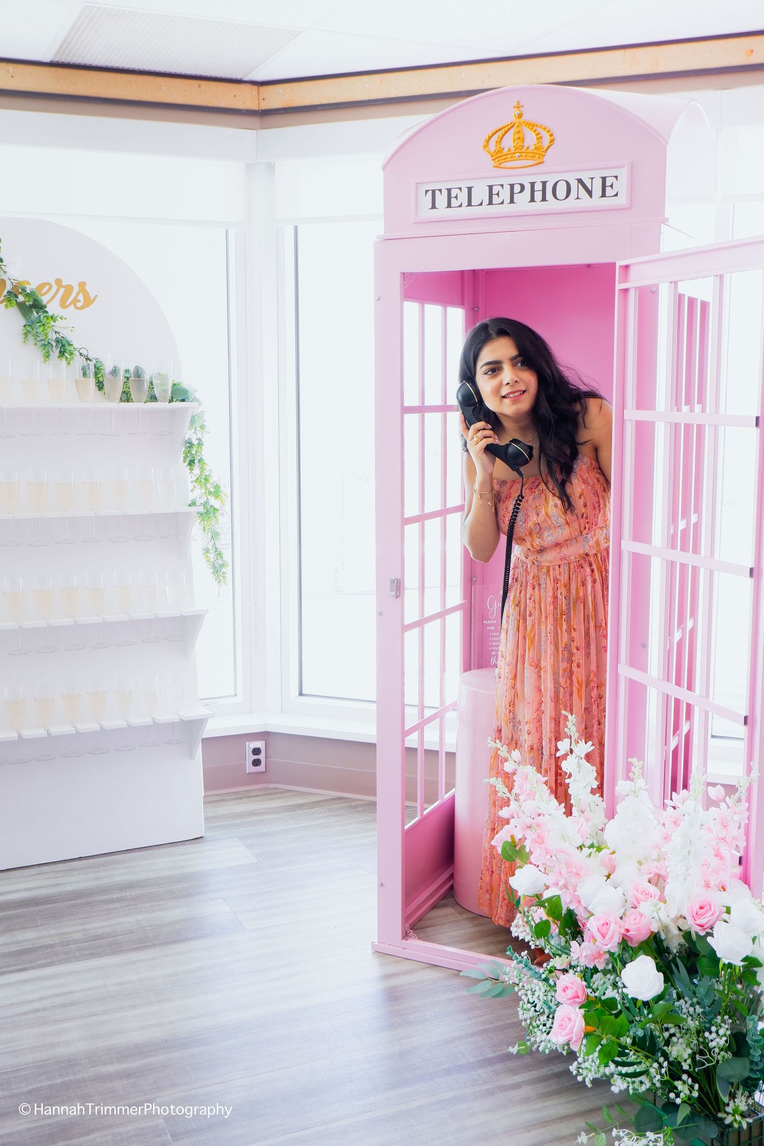 Woman in floral dress poses inside a decorative pink telephone booth at a bridal shower.