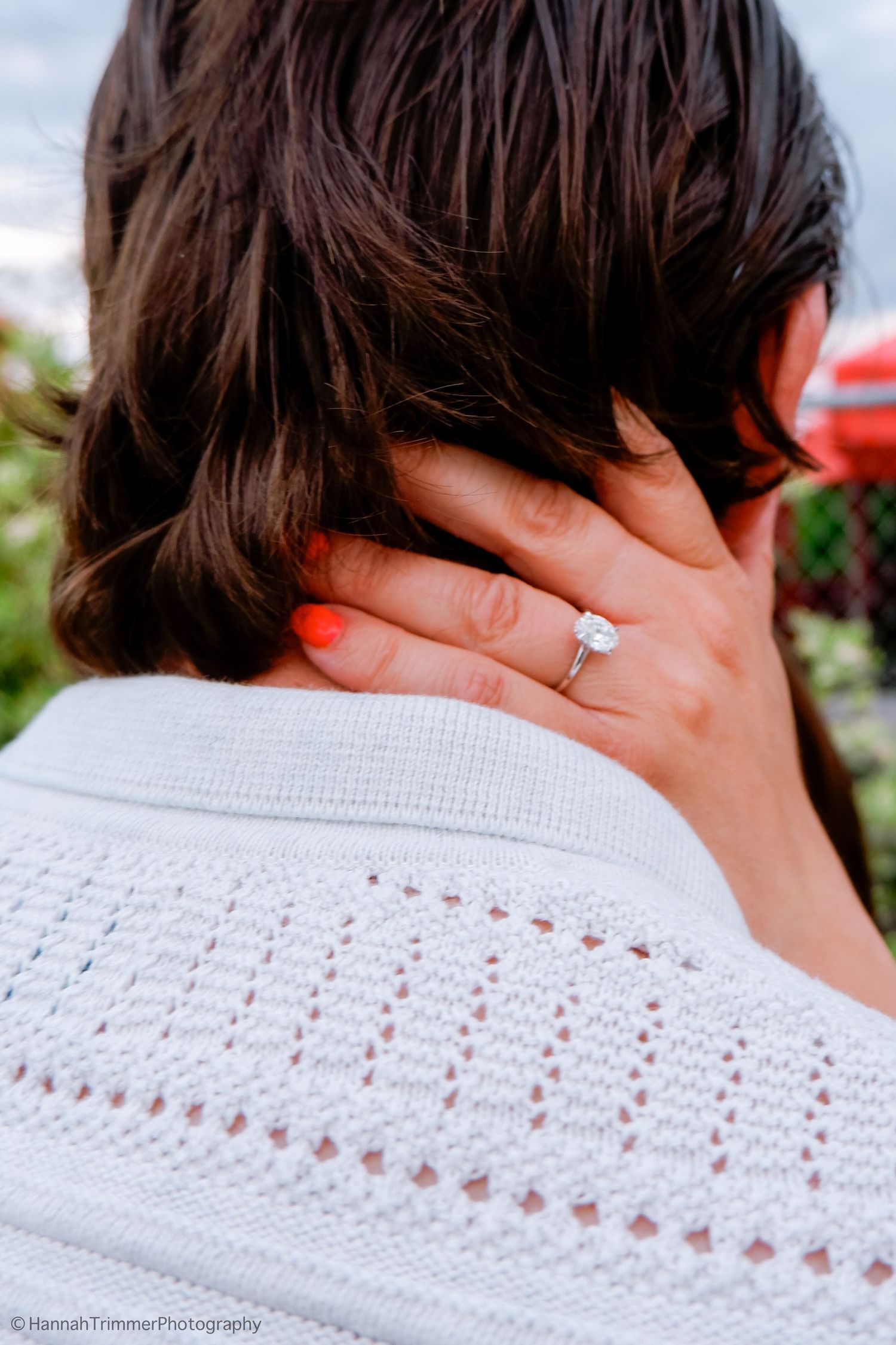 Close-up of engagement ring on woman's hand with orange nails resting on man's shoulder.