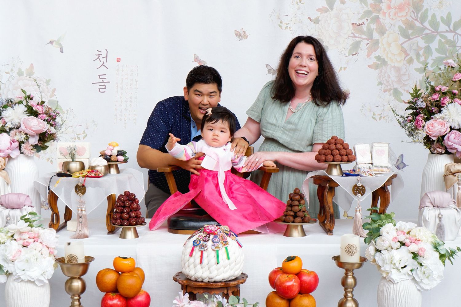 Family celebrating a baby's first birthday Dol party with traditional Korean hanbok dress and festive table spread.