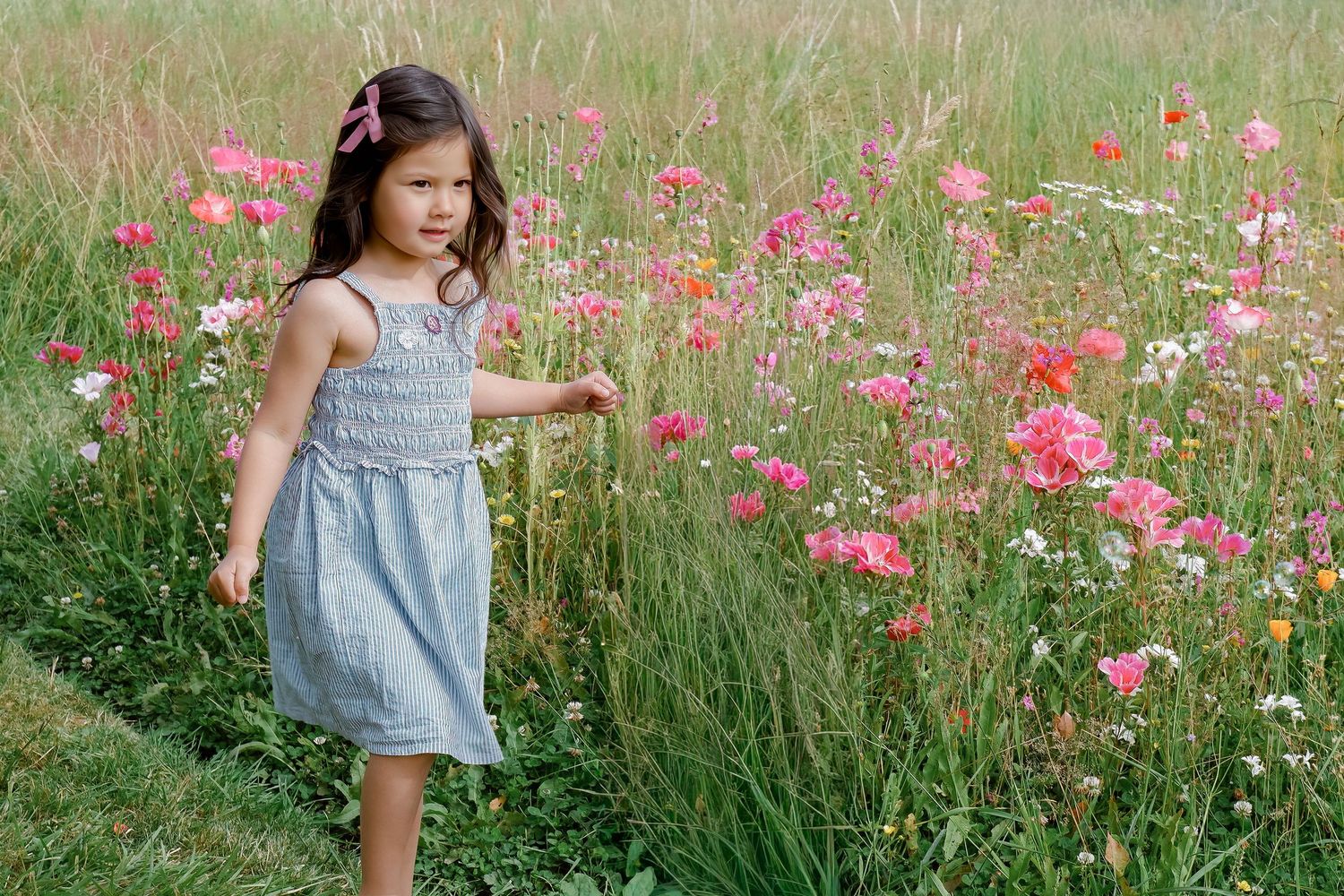 Young girl in a blue dress standing among vibrant pink wildflowers in a meadow.