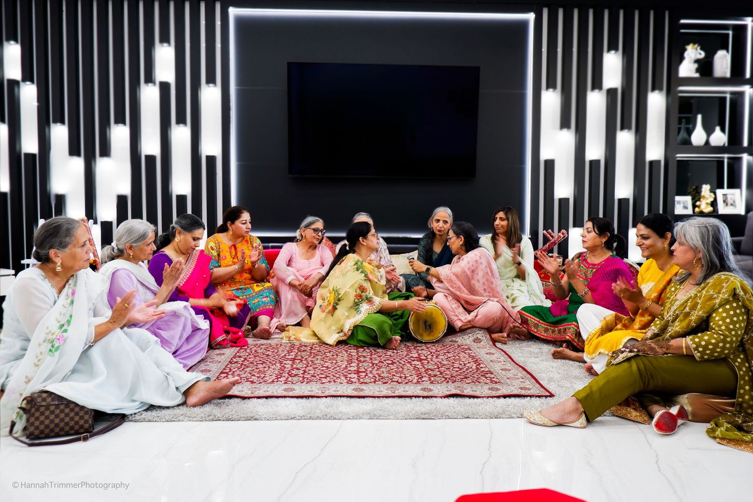 Group of women in vibrant sarees sitting on floor during traditional Indian wedding mehndi ceremony.