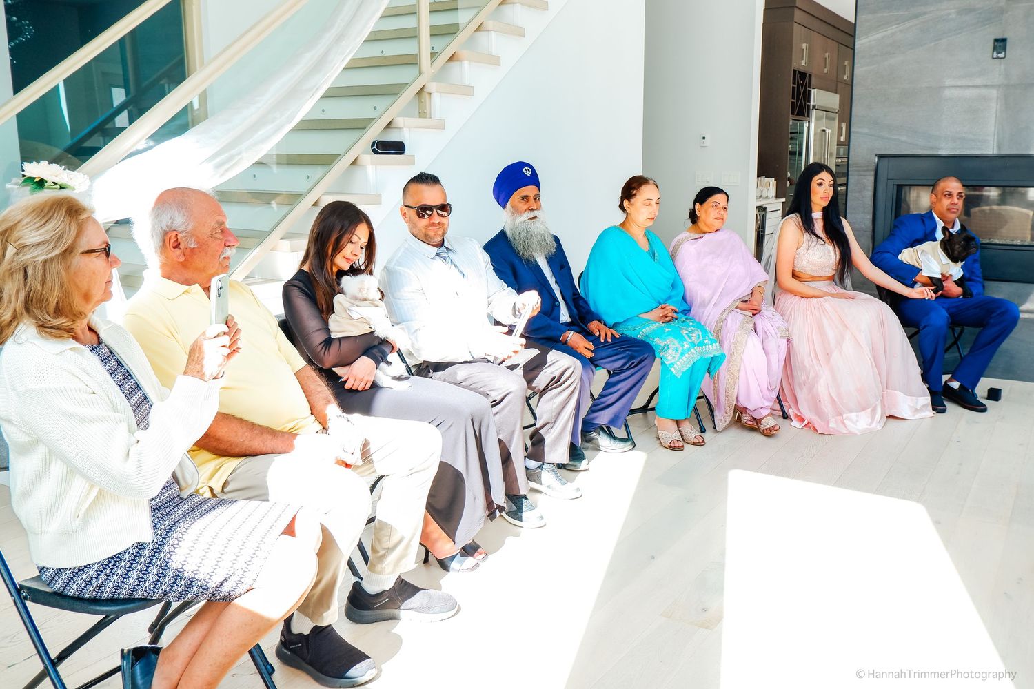 Diverse wedding guests in formal and traditional attire seated in a row during an intimate wedding ceremony.