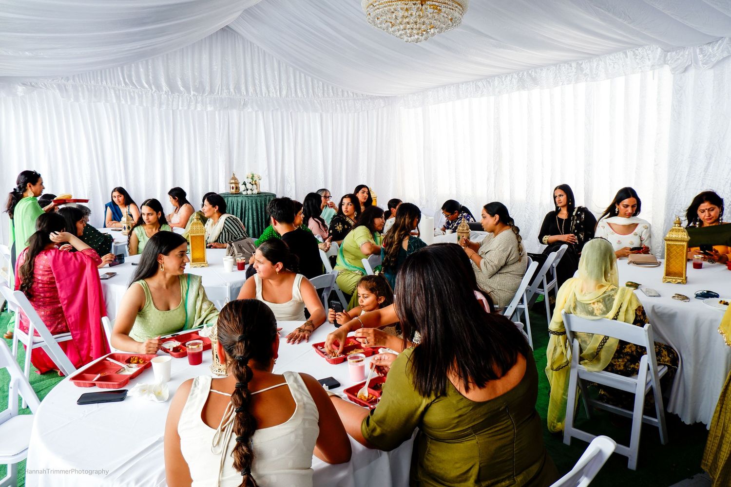 Guests in colorful traditional Indian attire dining together at tables during an indoor wedding reception.