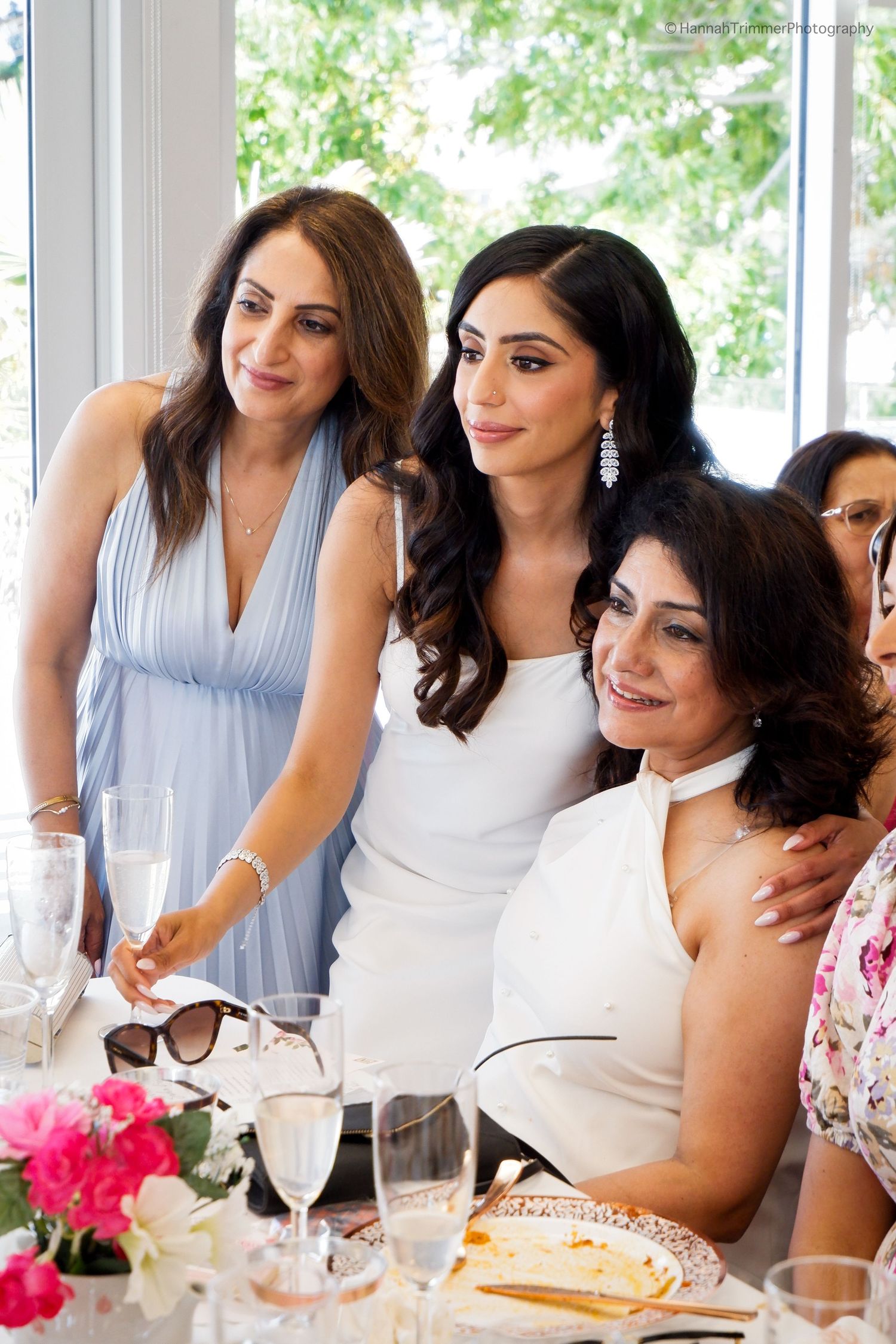 Bride to be in white dress smiles with guests during a bridal shower luncheon celebration.