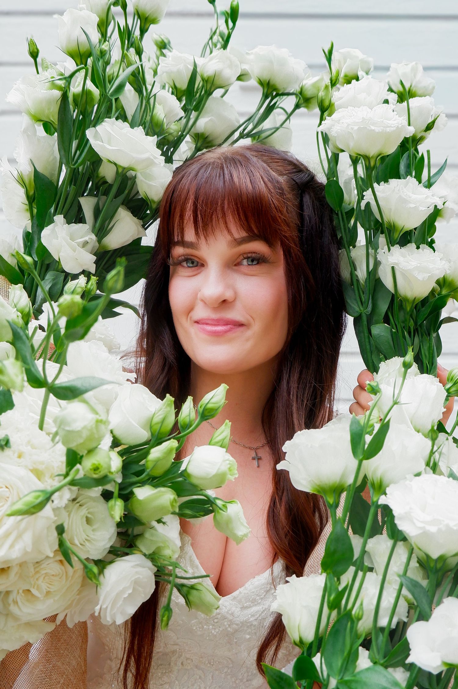 Smiling brunette bride surrounded by white roses and lisianthus flowers in a floral frame, wearing a white dress.