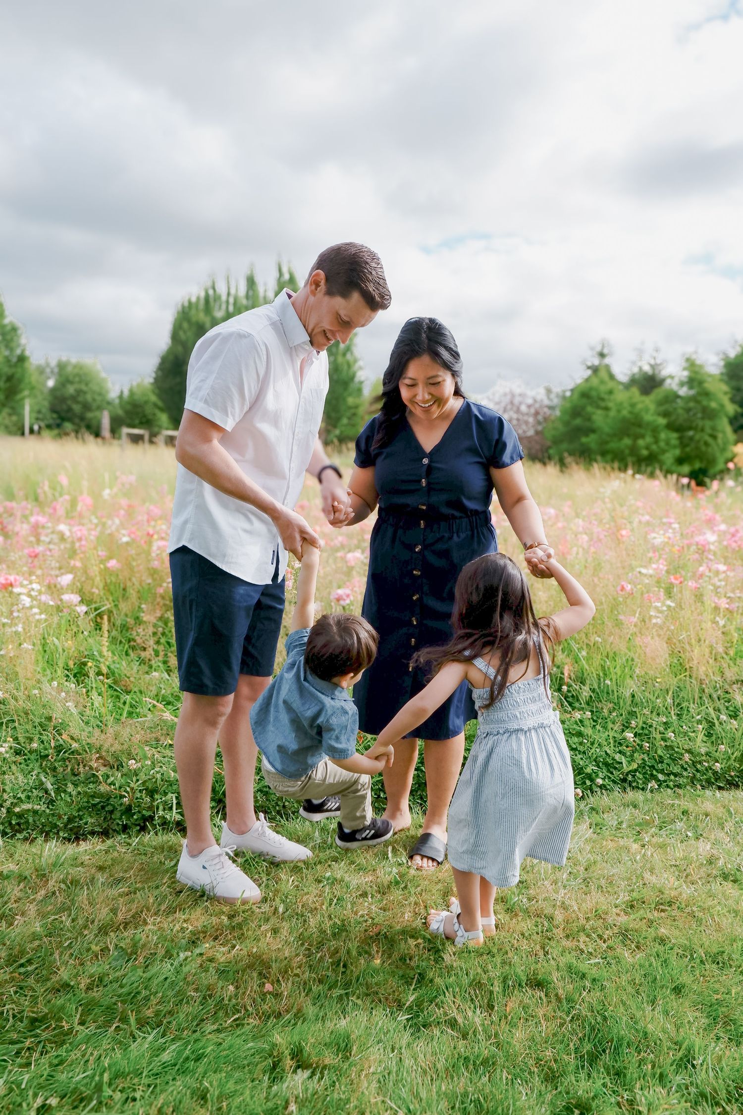 A cheerful family of four plays together in a blooming wildflower meadow on a cloudy day.