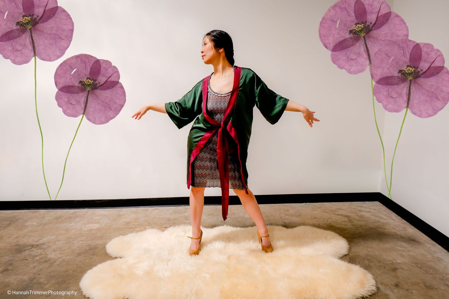 Woman poses gracefully in a green satin kimono robe on a fluffy rug with floral wall art.