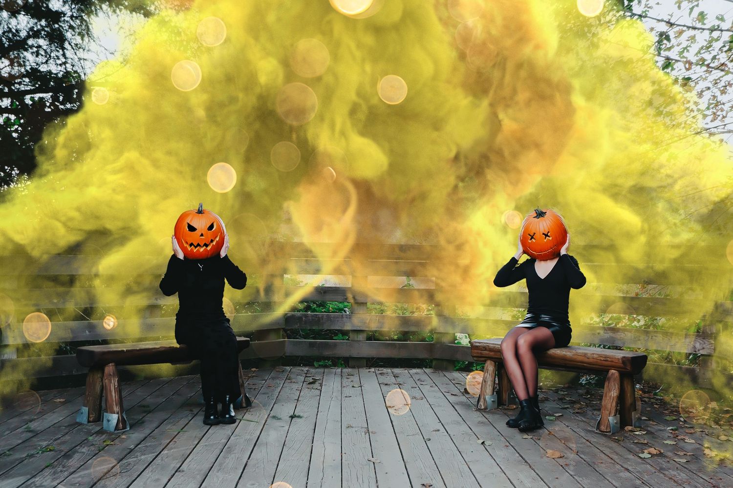 Two people wearing jack-o-lantern pumpkin heads sit on benches surrounded by yellow Halloween smoke outdoors.