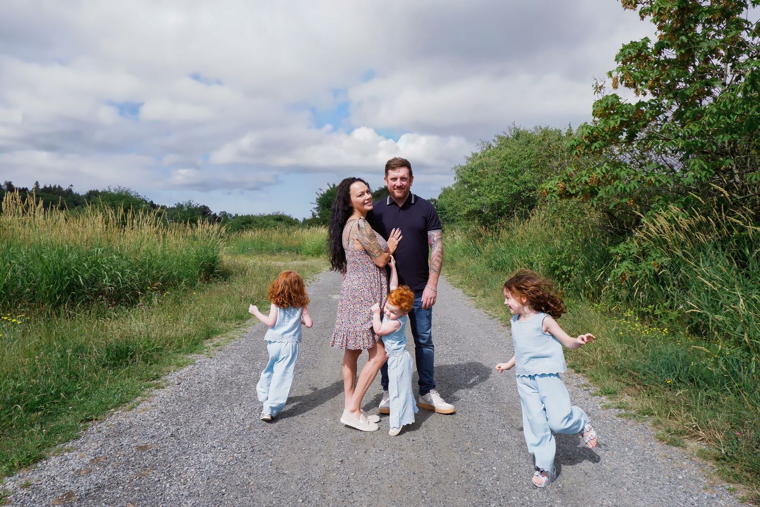 Happy family of five laughing and playing together on a gravel country road outdoors.