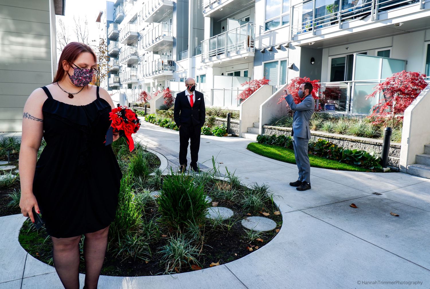 Wedding party in masks poses in modern apartment courtyard with red bow decorations during COVID pandemic.