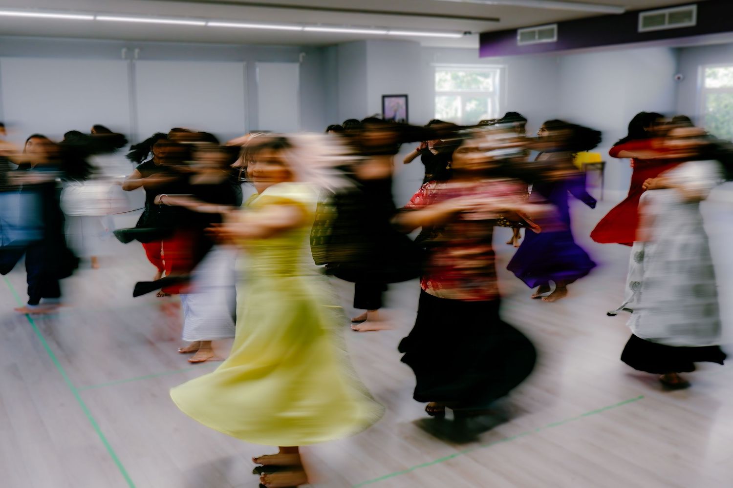 Motion blur photo of women dancing in colorful traditional outfits in a dance studio.