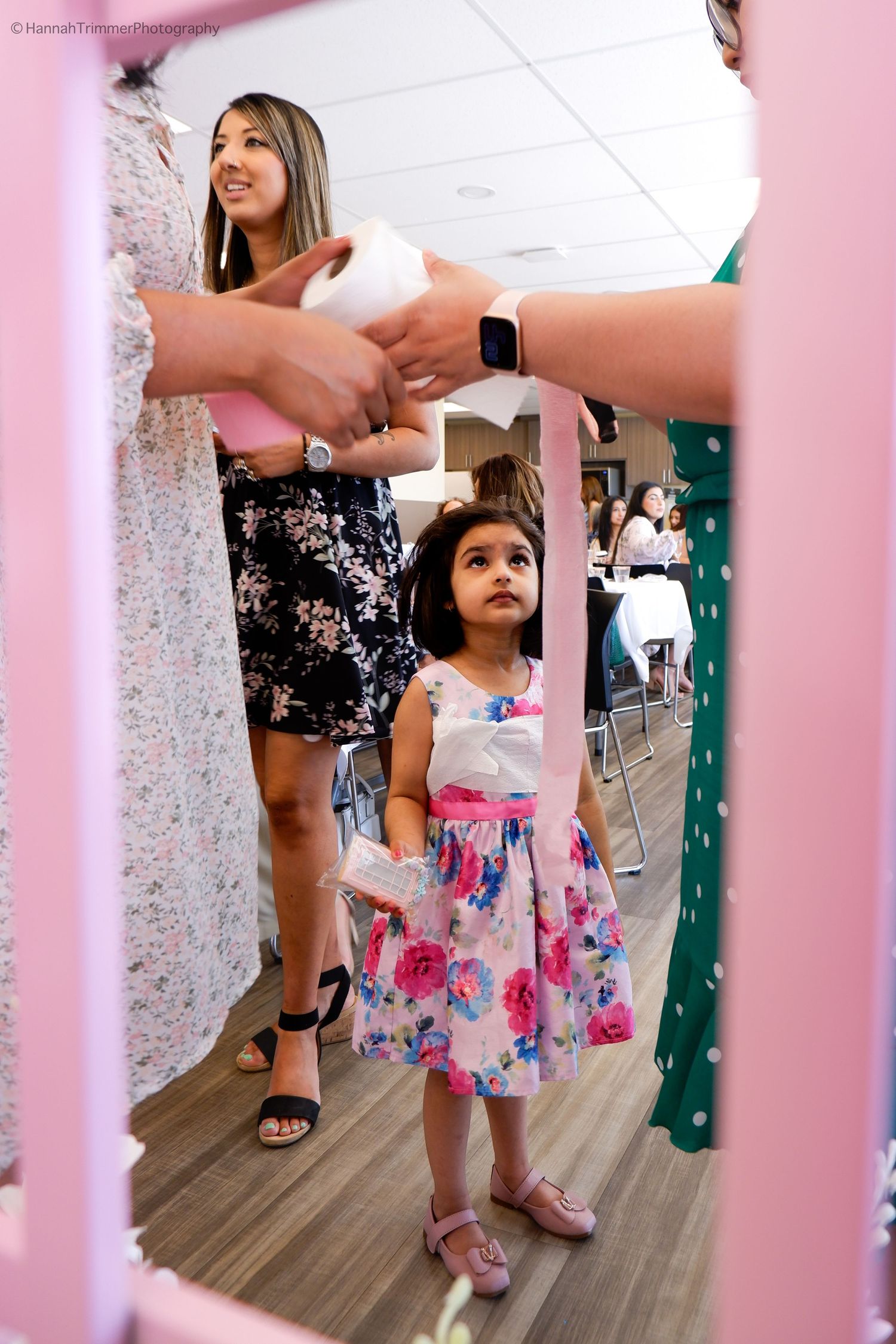 Adorable little girl in floral dress watches a toilet paper bridal game at a bridal shower.