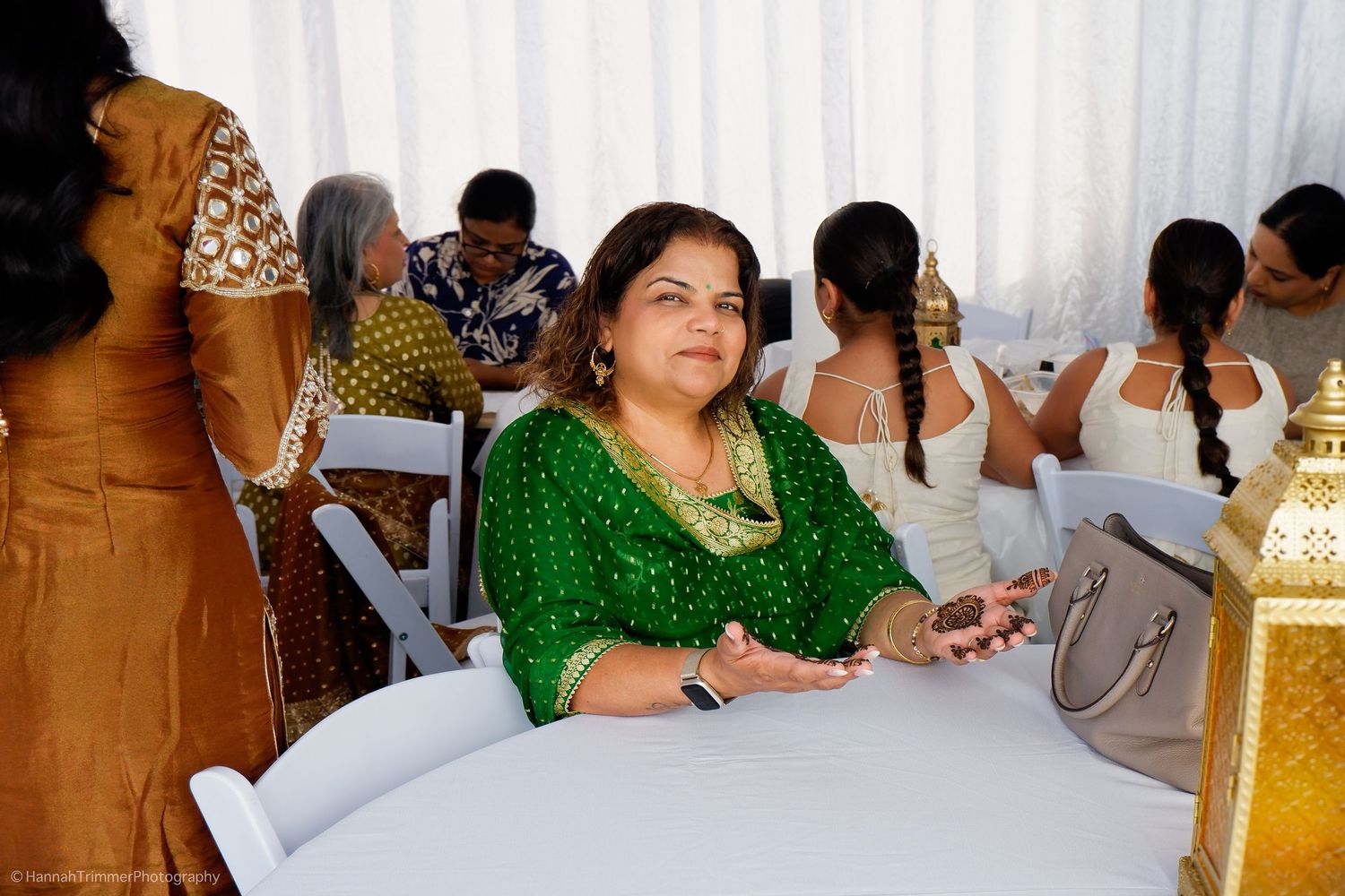 Woman in green salwar kameez with gold jewelry seated at an Indian wedding reception under a tent.
