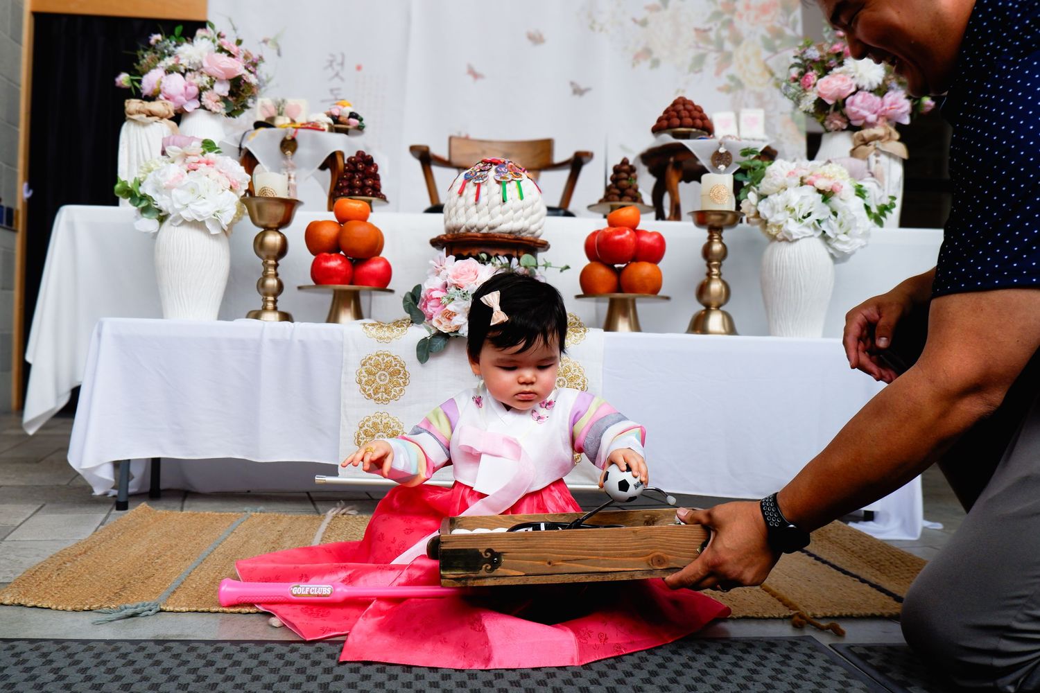 Baby girl in hanbok sits at doljabi table during Korean first birthday dol celebration ceremony.