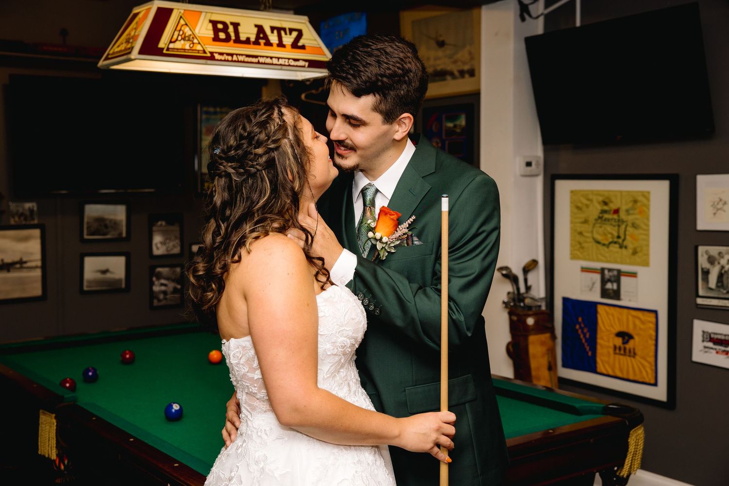 Bride and groom share a romantic moment holding a pool cue near a Blatz billiards table at their wedding reception.