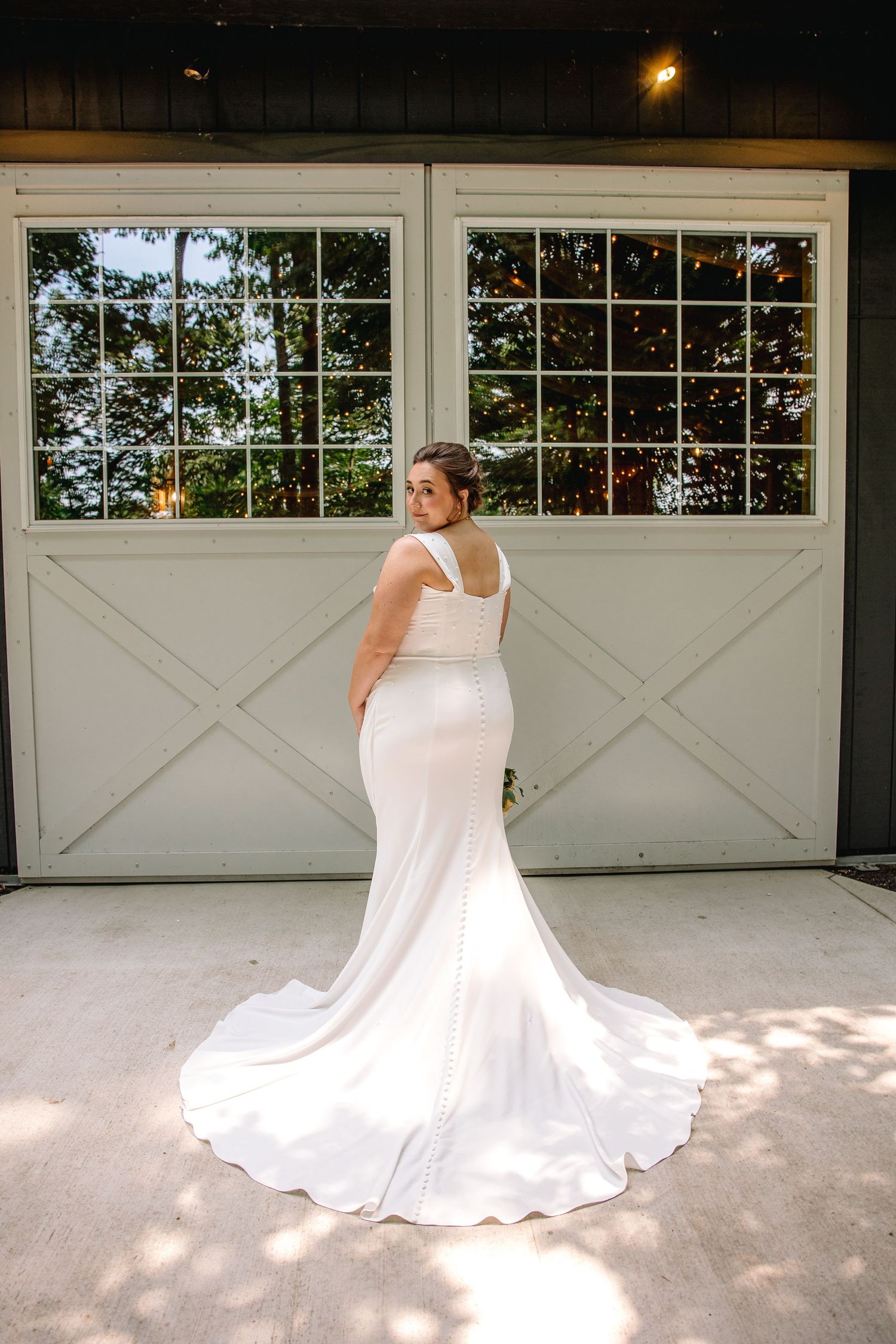 Bride in elegant white mermaid wedding gown with train poses in front of white barn doors.