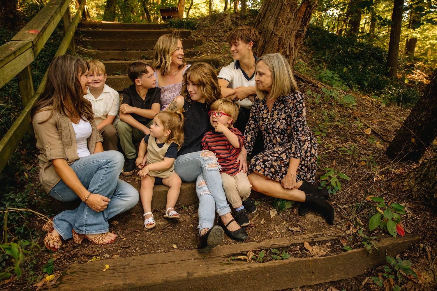 Large family group with children and adults sitting together on wooden steps in a lush green forest setting.