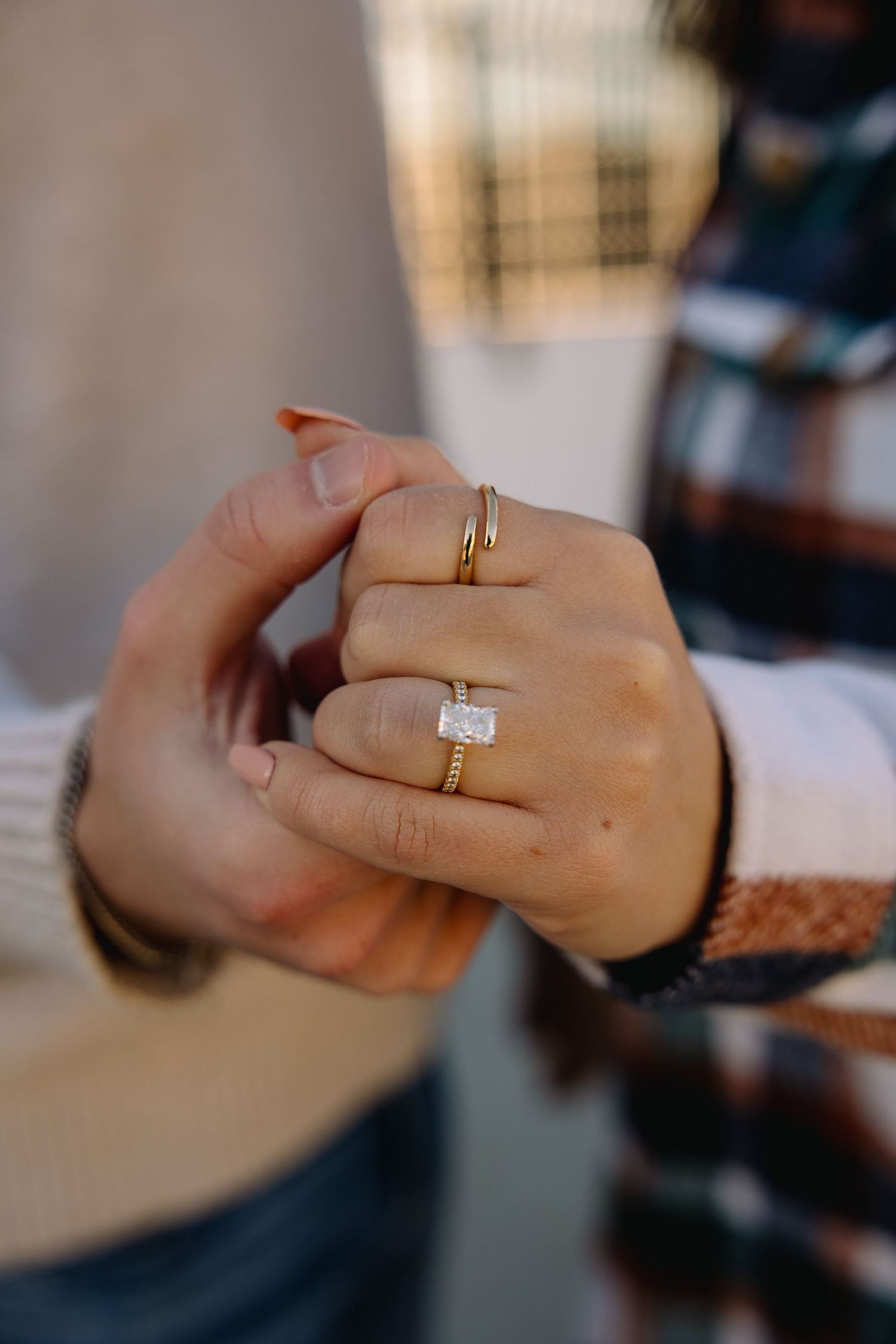 Close-up of a woman's hand wearing a gold emerald-cut diamond engagement ring with stacked gold bands.