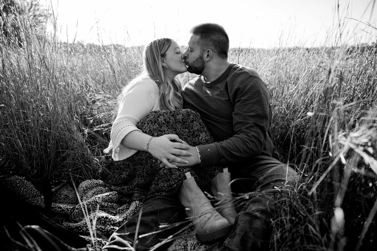 Black and white photo of a couple kissing while sitting in a field of tall grass.
