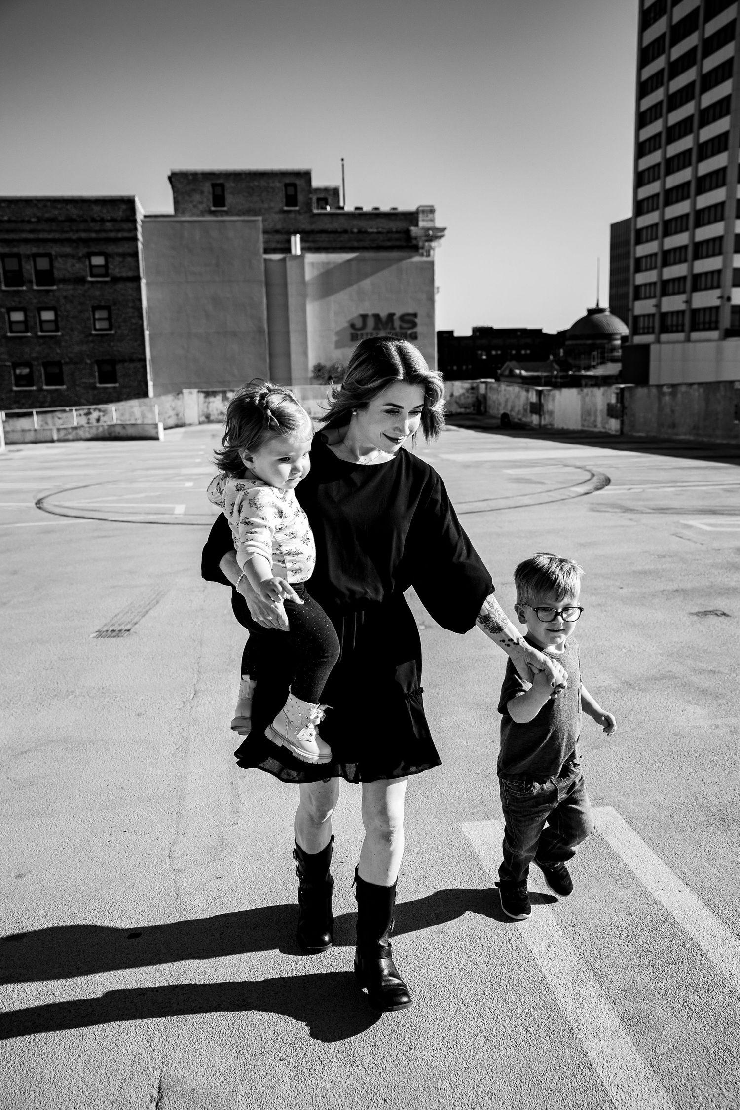 Black and white photo of a woman carrying a toddler while holding a young boy's hand on a rooftop.