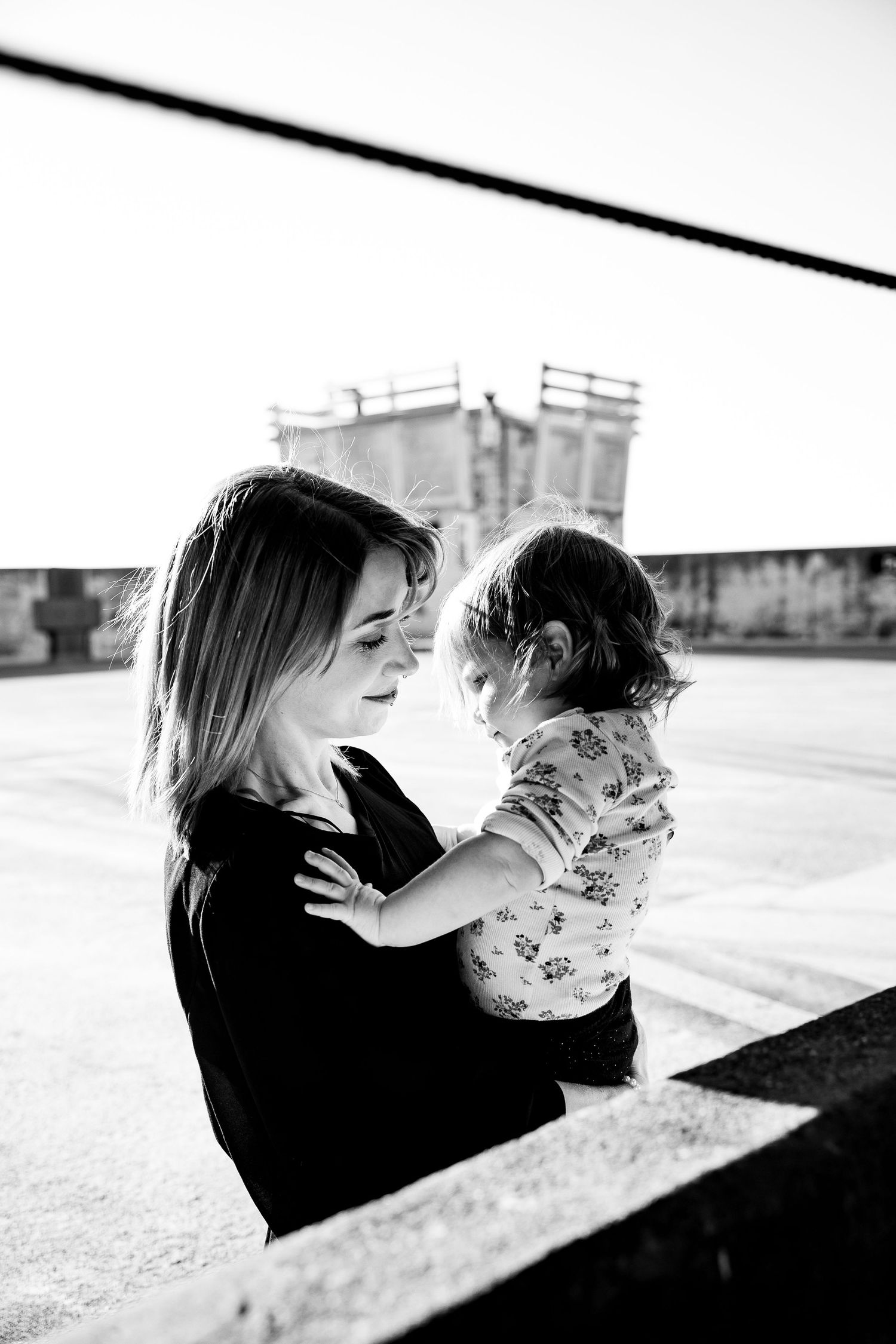 Black and white photo of a young mother tenderly holding her toddler outdoors on a rooftop.