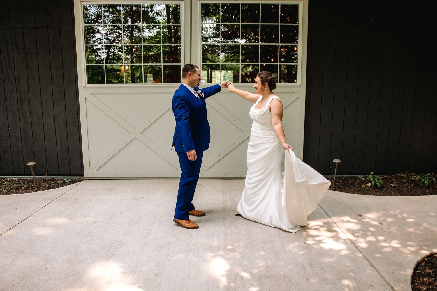 Bride and groom share a joyful first dance moment outside a black barn venue, bride twirling in white gown.
