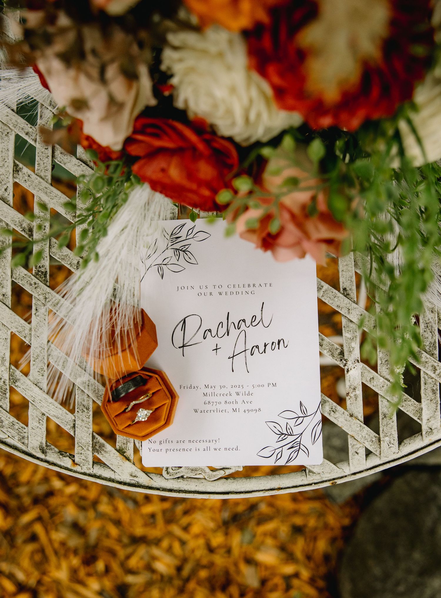 Wedding invitation for Rachael and Aaron displayed with an amber ring box and colorful floral arrangement on a lattice table.