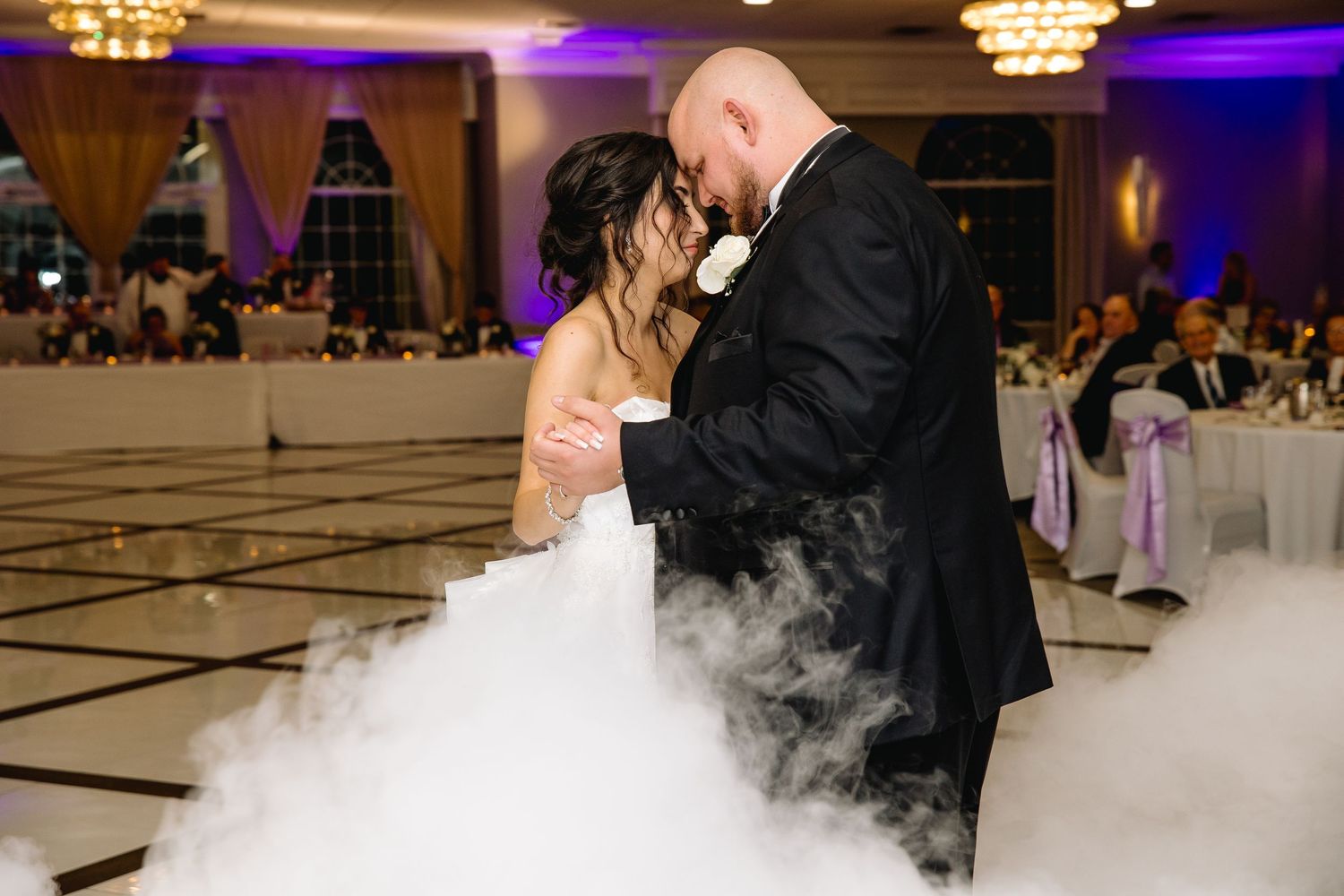 Bride and groom share first dance surrounded by romantic fog machine effects in an elegant wedding reception venue.