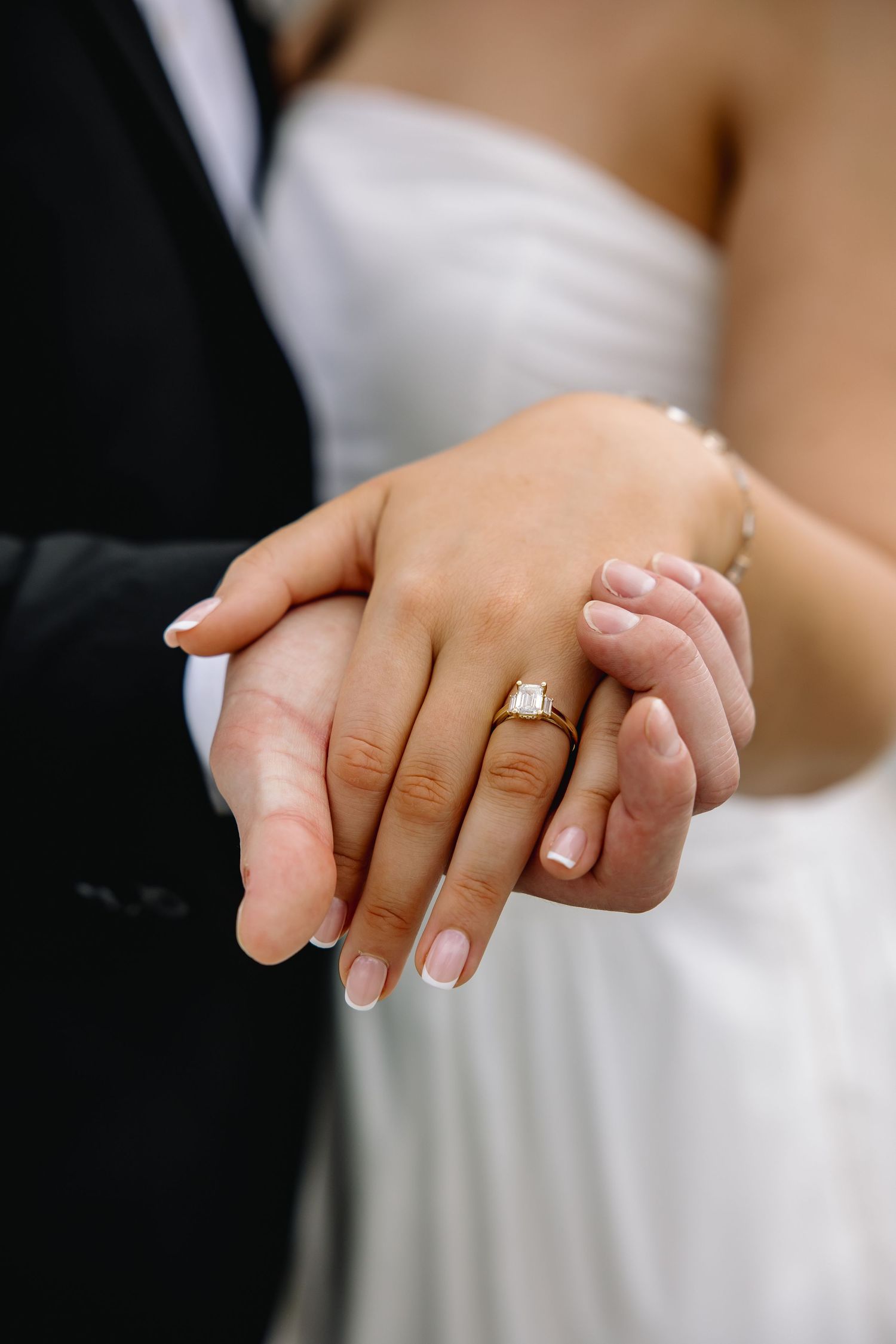 Bride and groom holding hands displaying a gold diamond engagement ring on wedding day.