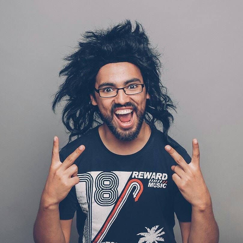 A picture of Cristian as he holds up peace signs and is wearing a big black wig.