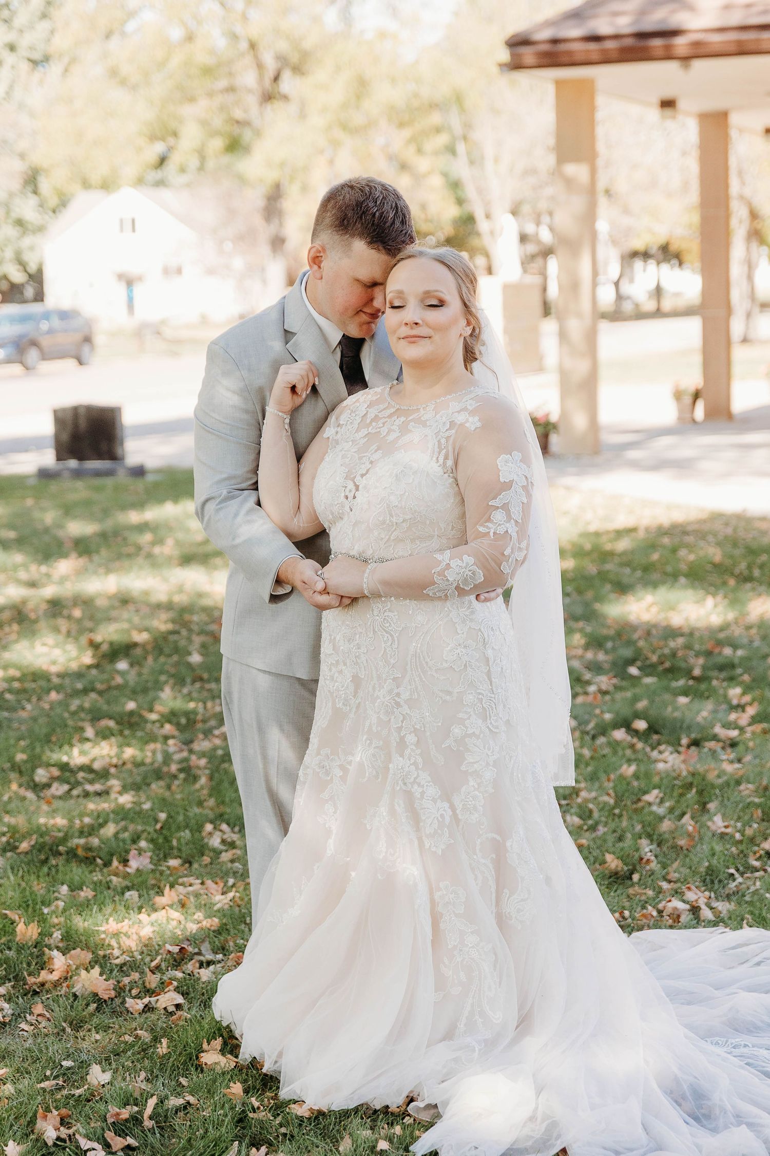 Romantic outdoor wedding scene with couple in elegant attire featuring a flowing white lace gown and grey suit.